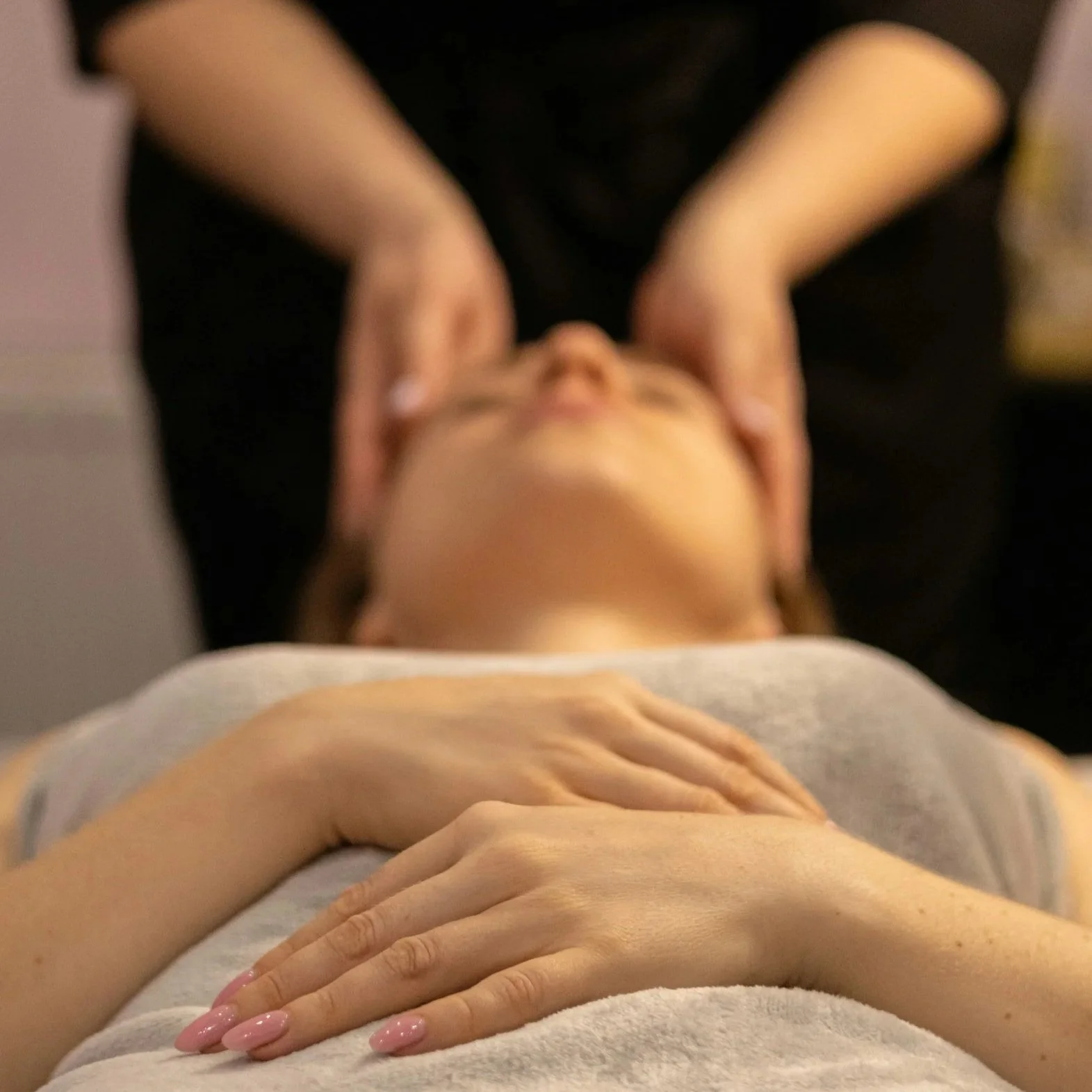 A woman lying on a massage table, receiving a CranioSacral Therapy treatment, with her hands resting on her chest and her eyes closed.