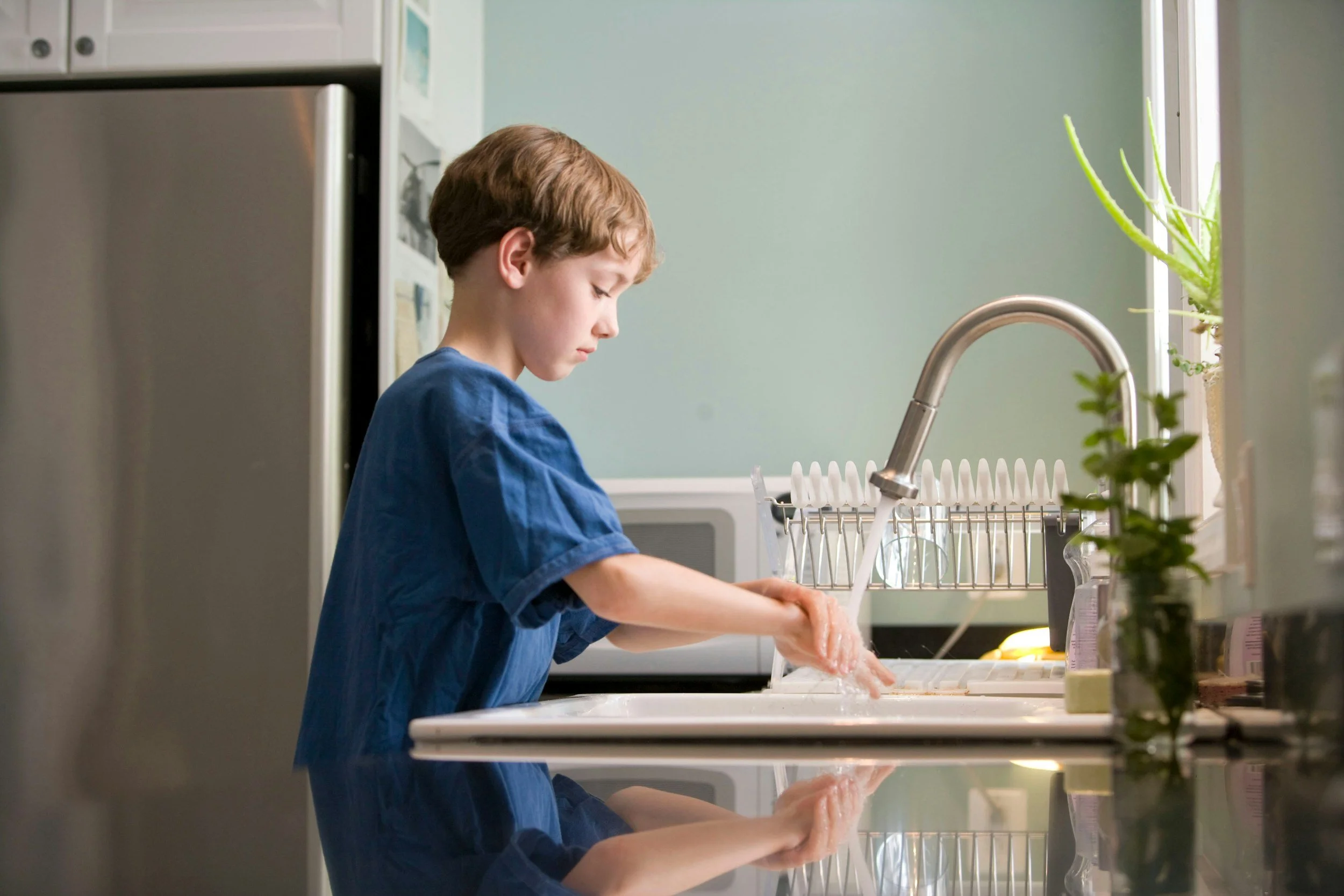 A young boy washing his hands at the kitchen sink.