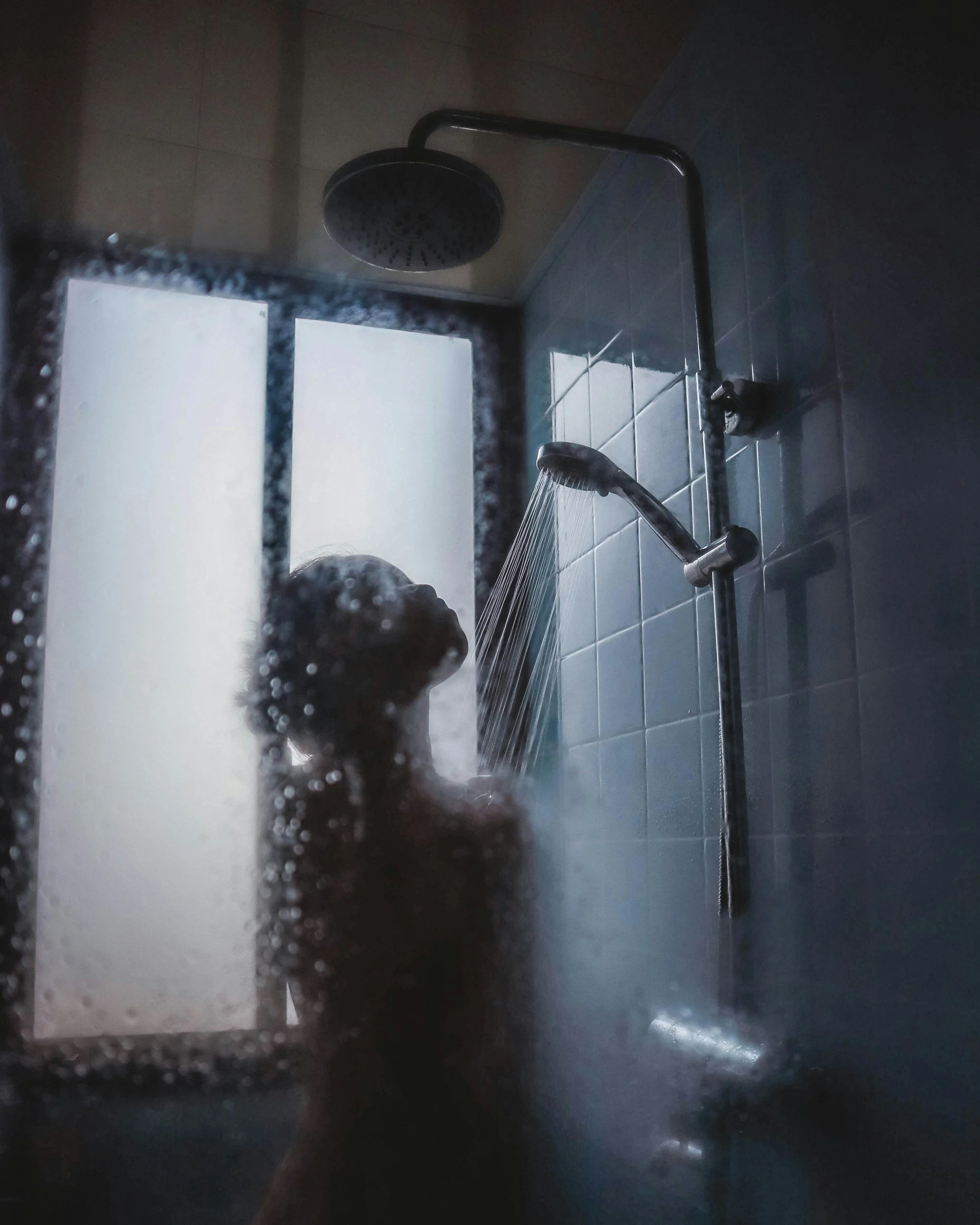 Person taking a shower behind a steamy glass door in a bathroom, with water running from the showerhead.