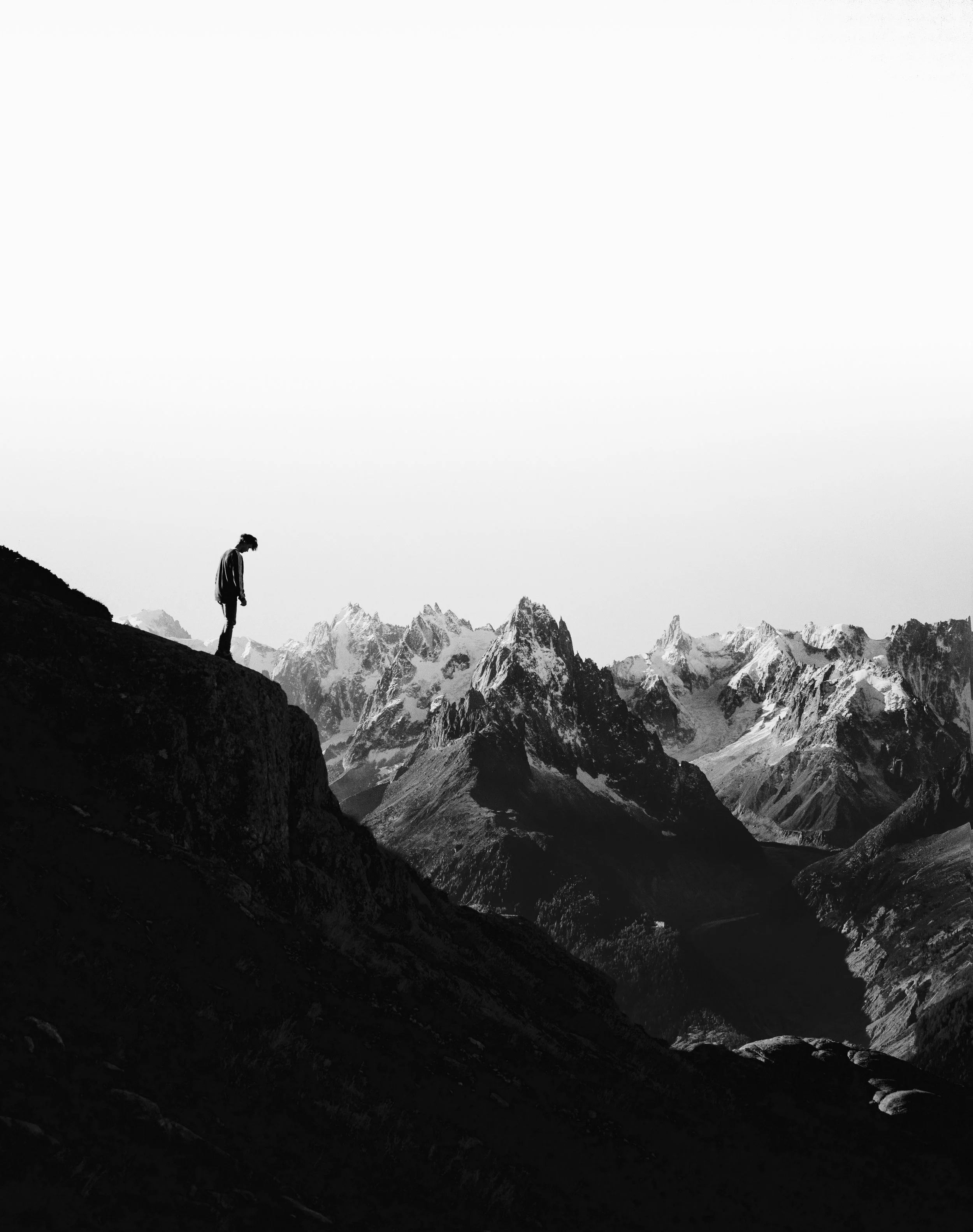 Person standing alone on a cliff overlooking mountain peaks, representing risk awareness and taking safety seriously.
