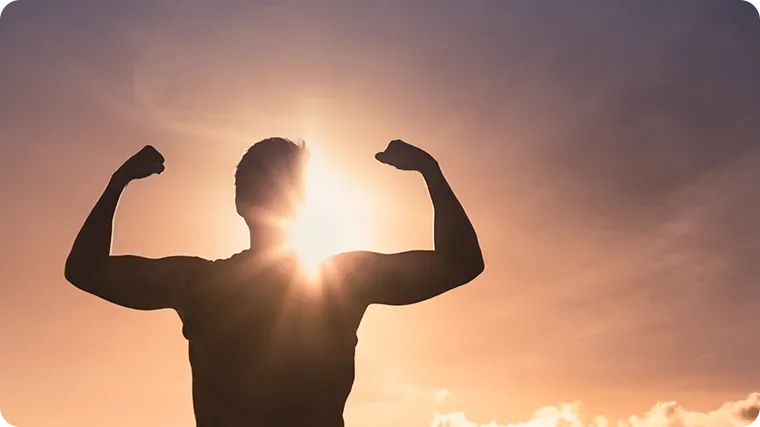 Silhouette of a person flexing arm muscles at sunset or sunrise.