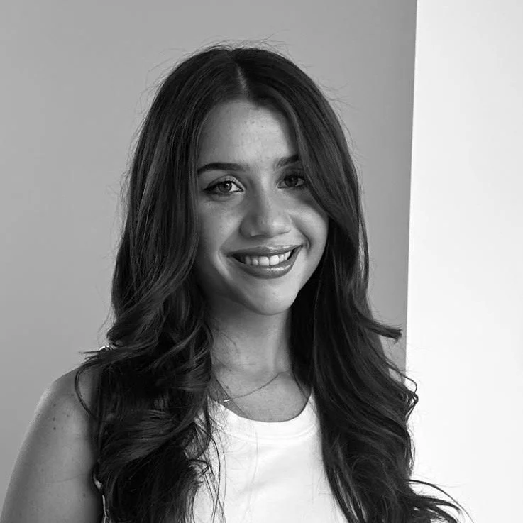 Black and white photo of a young woman with long wavy hair, smiling and wearing a sleeveless top.