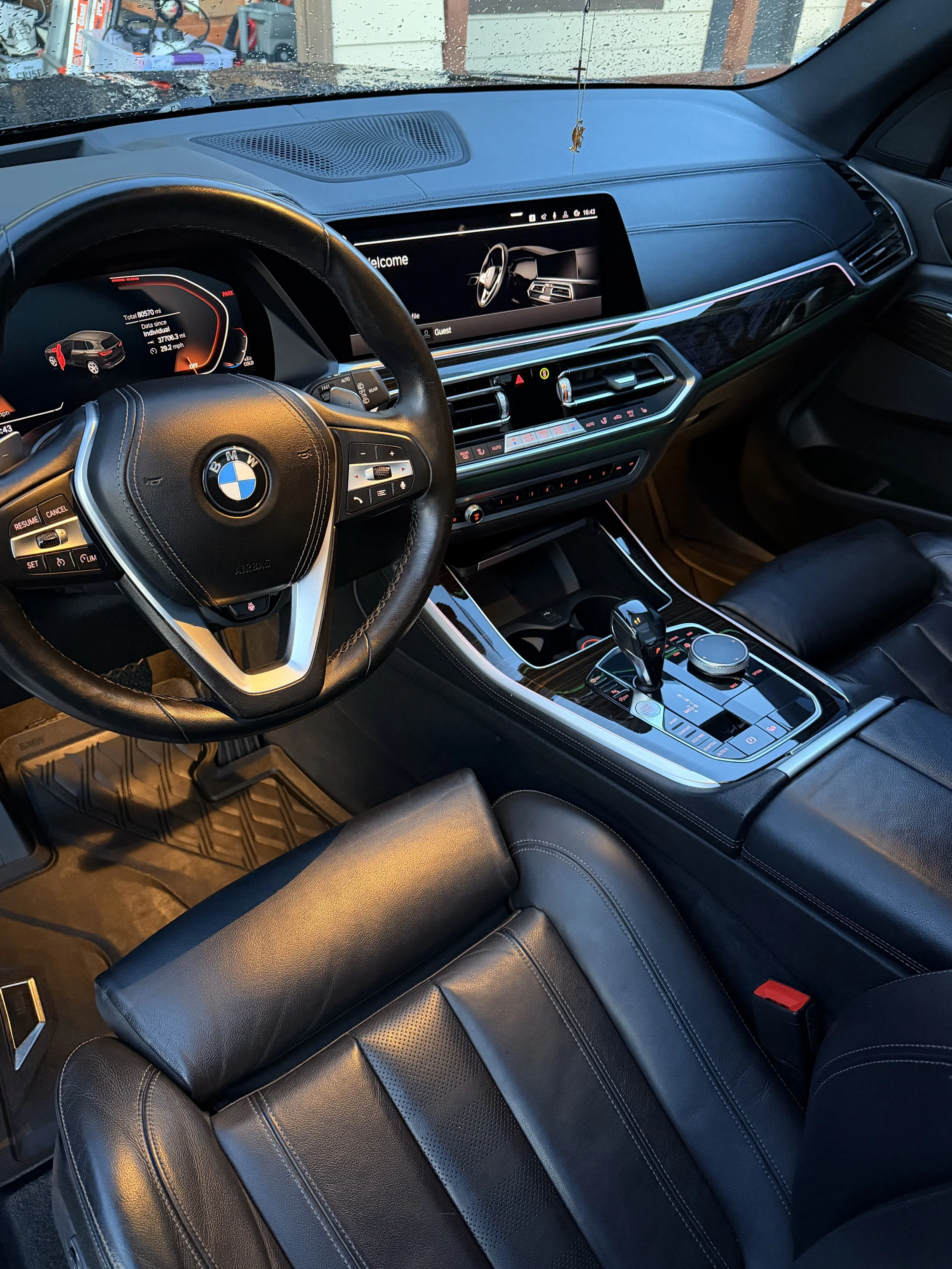 The interior of a BMW vehicle showing the steering wheel, dashboard, gear shift, and central control area with electronic displays, all in black leather.