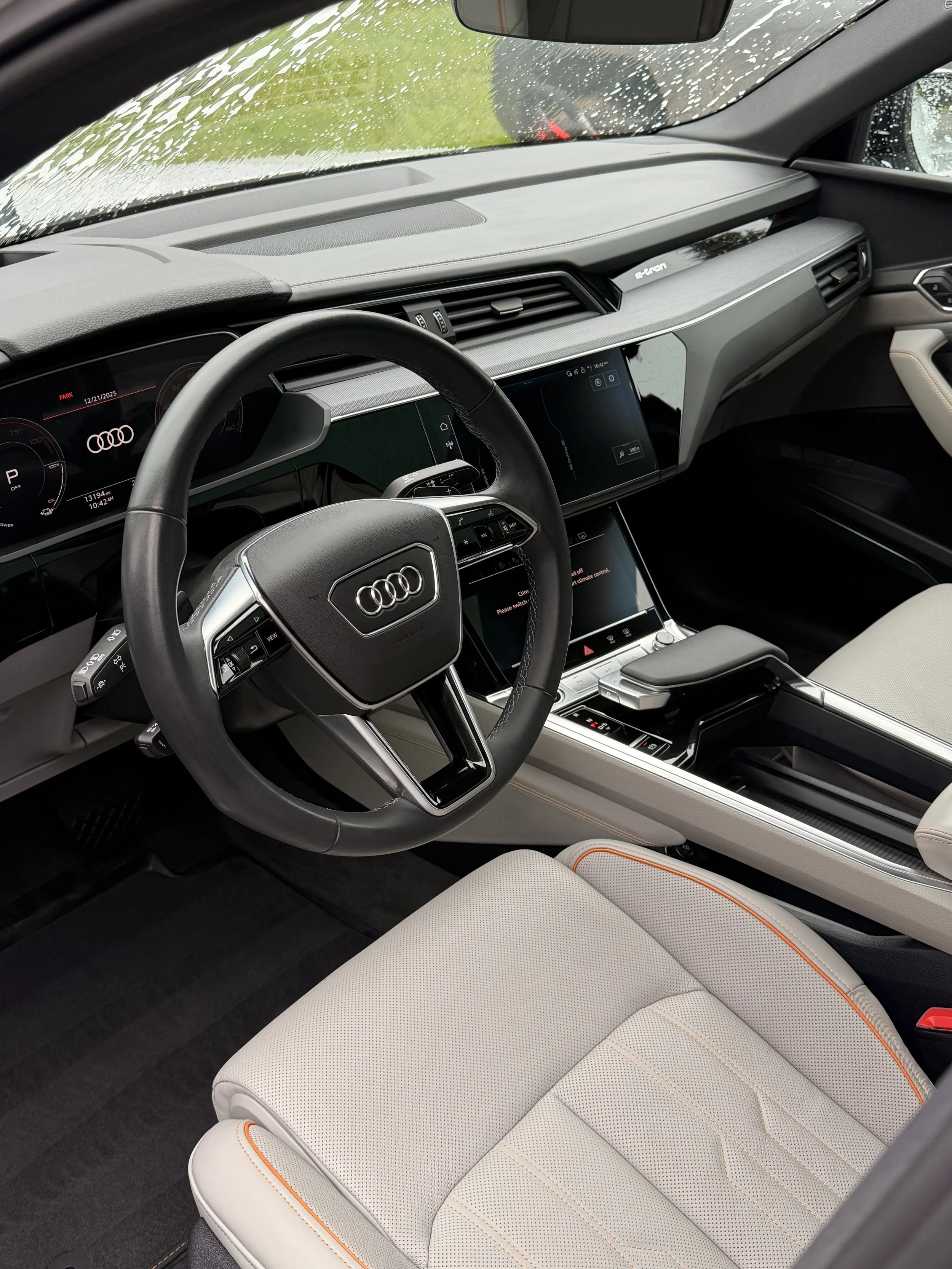 Interior view of an Audi vehicle showing the steering wheel, digital dashboard, and center console with touchscreen displays and gear shift.