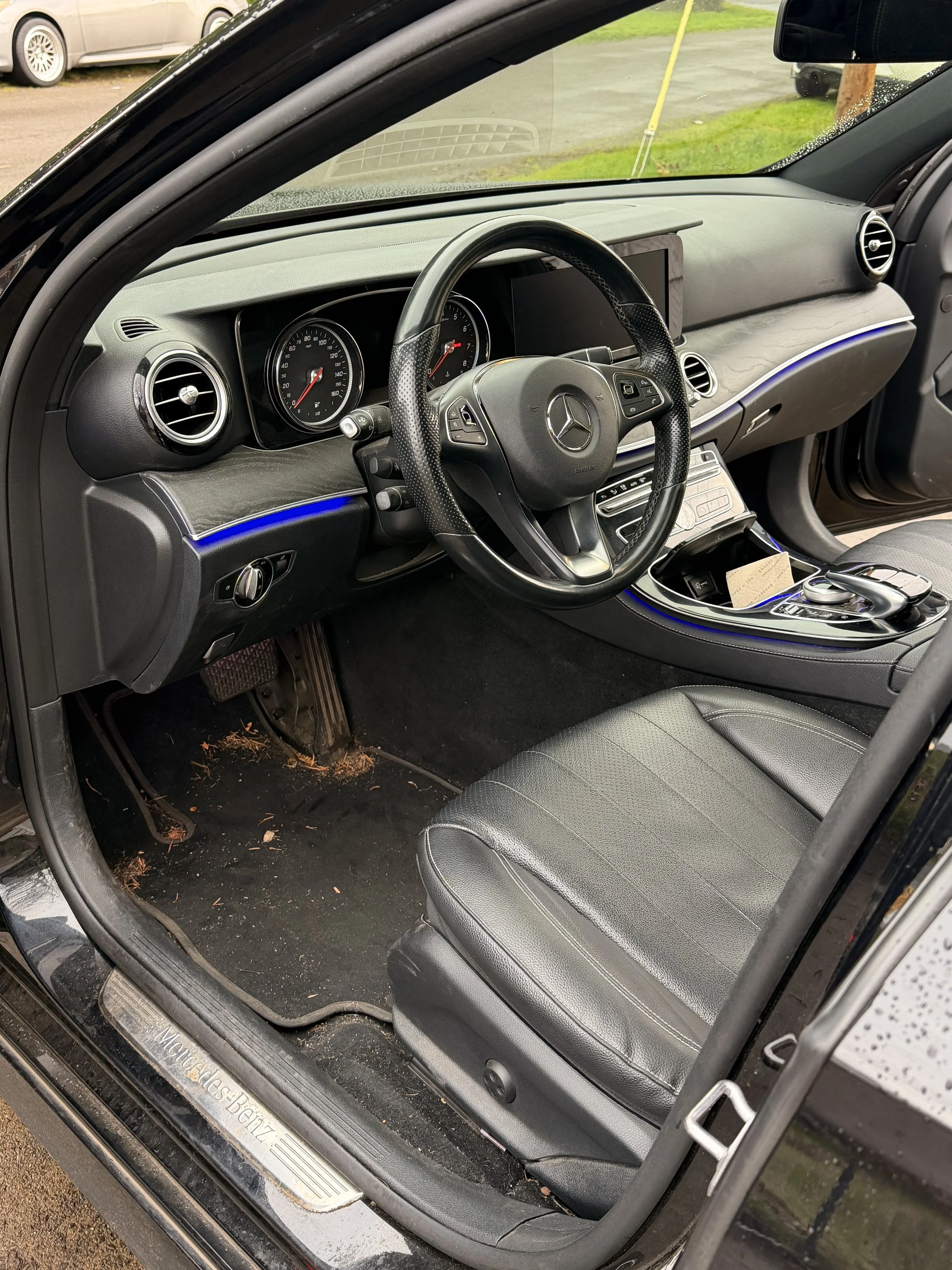 Interior of a black Mercedes-Benz car showing the dashboard, steering wheel, front seat, and floor area with some debris.
