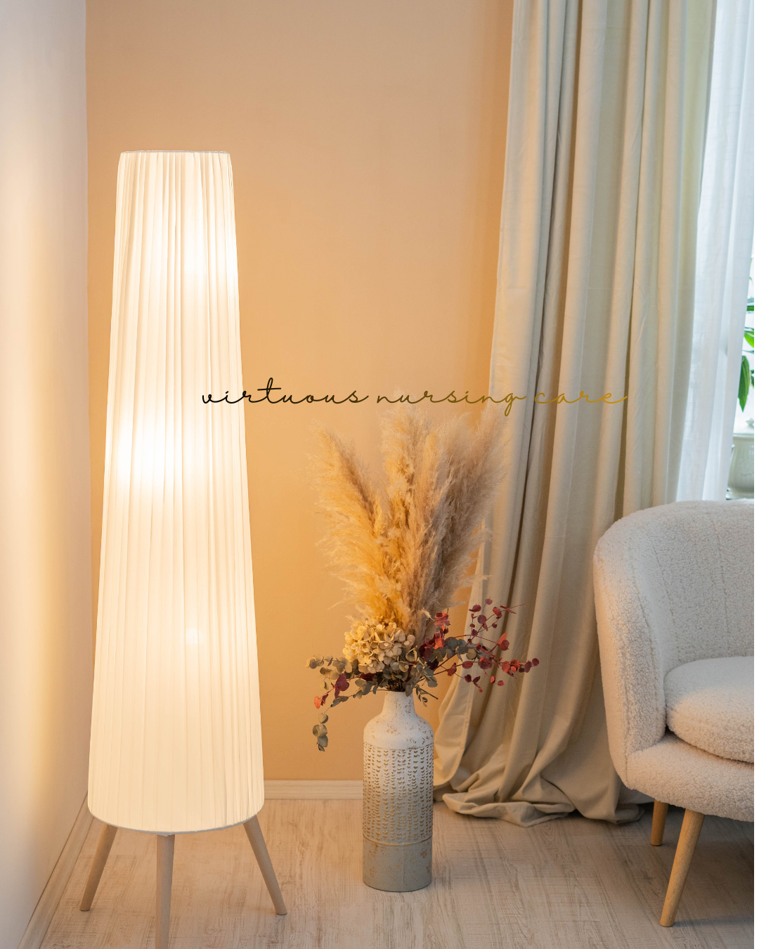 Room corner with a tall white floor lamp, a vase with pampas grass and flowers, cream curtains, and a white textured armchair.