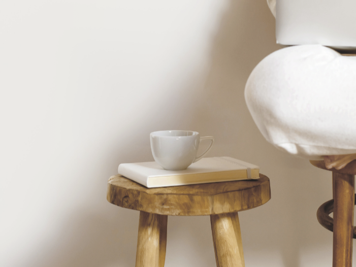 White coffee mug placed on top of a closed book on a small wooden stool.