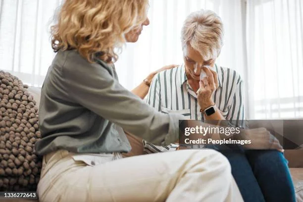 A counselor consoling another woman on a couch who is tearful