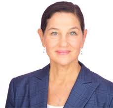 Professional woman with short dark hair, wearing a blue blazer, smiling against a white background.