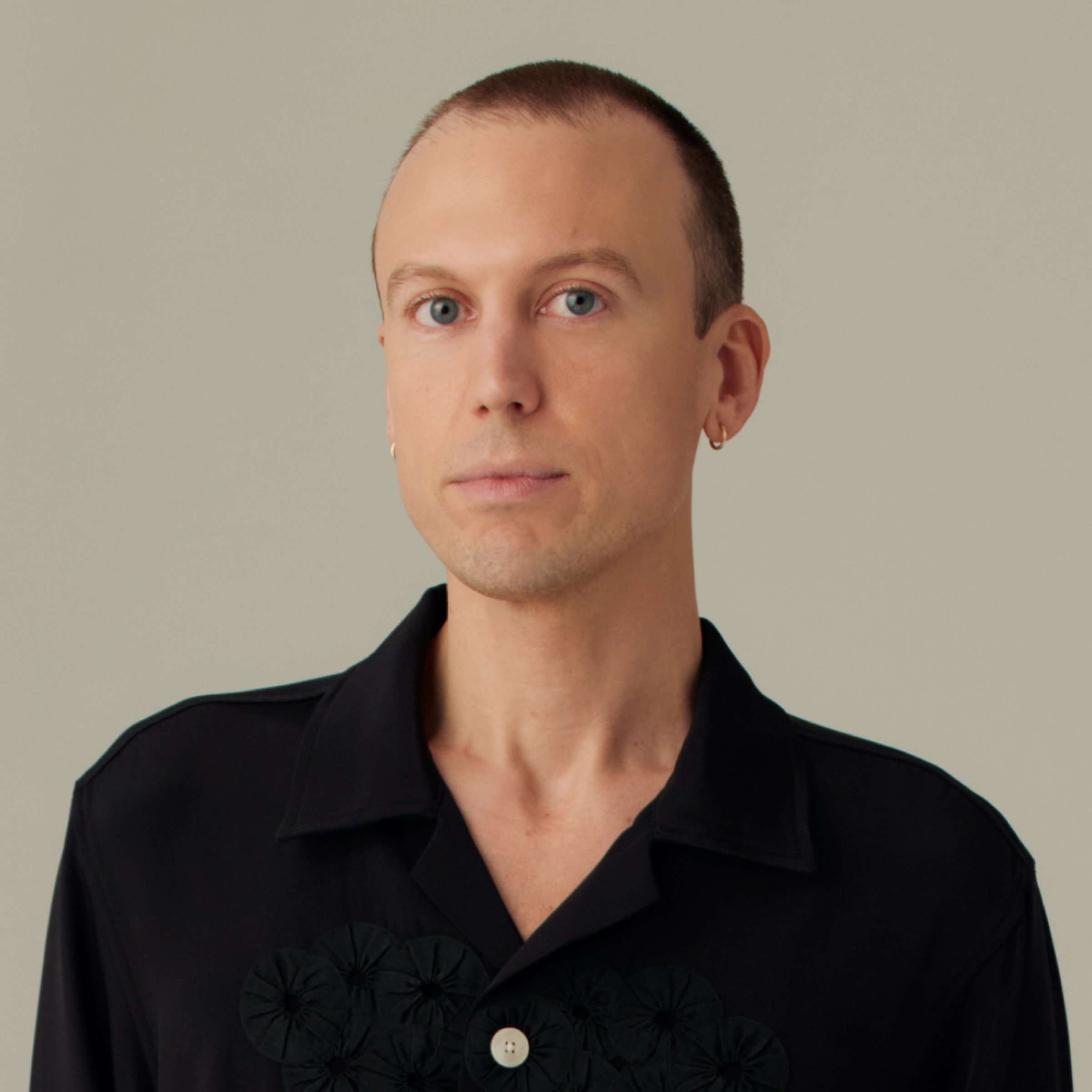 Portrait of Michael Diaz-Griffith in a black embroidered shirt against a warm gray background. Photograph by Alan David Padilla.