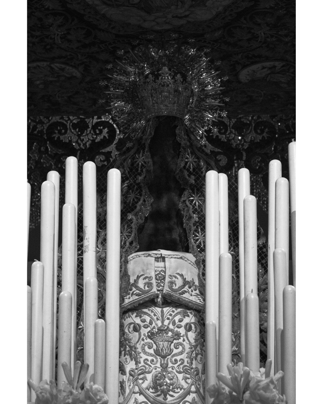 A ghostly stillness in the center of the frame. The heavy, ambient silence of the empty space left on the paso where the Virgen de la Macarena stands, illuminated only by rows of burning candles fading into absolute dark.

Una quietud casi fantasmal 