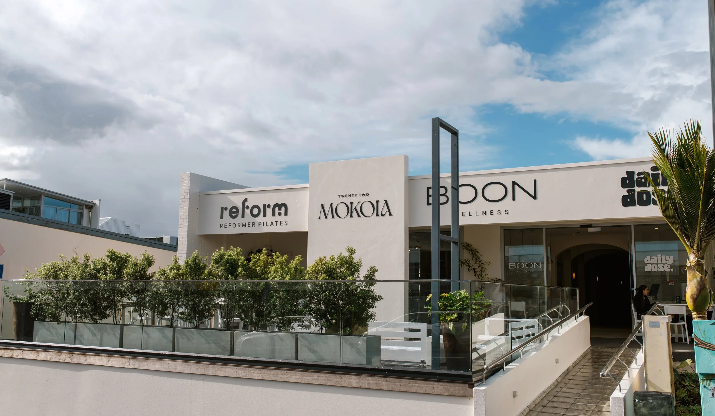 Exterior of a modern wellness center with signs for Reform Pilates, MOKOA, and BOON.