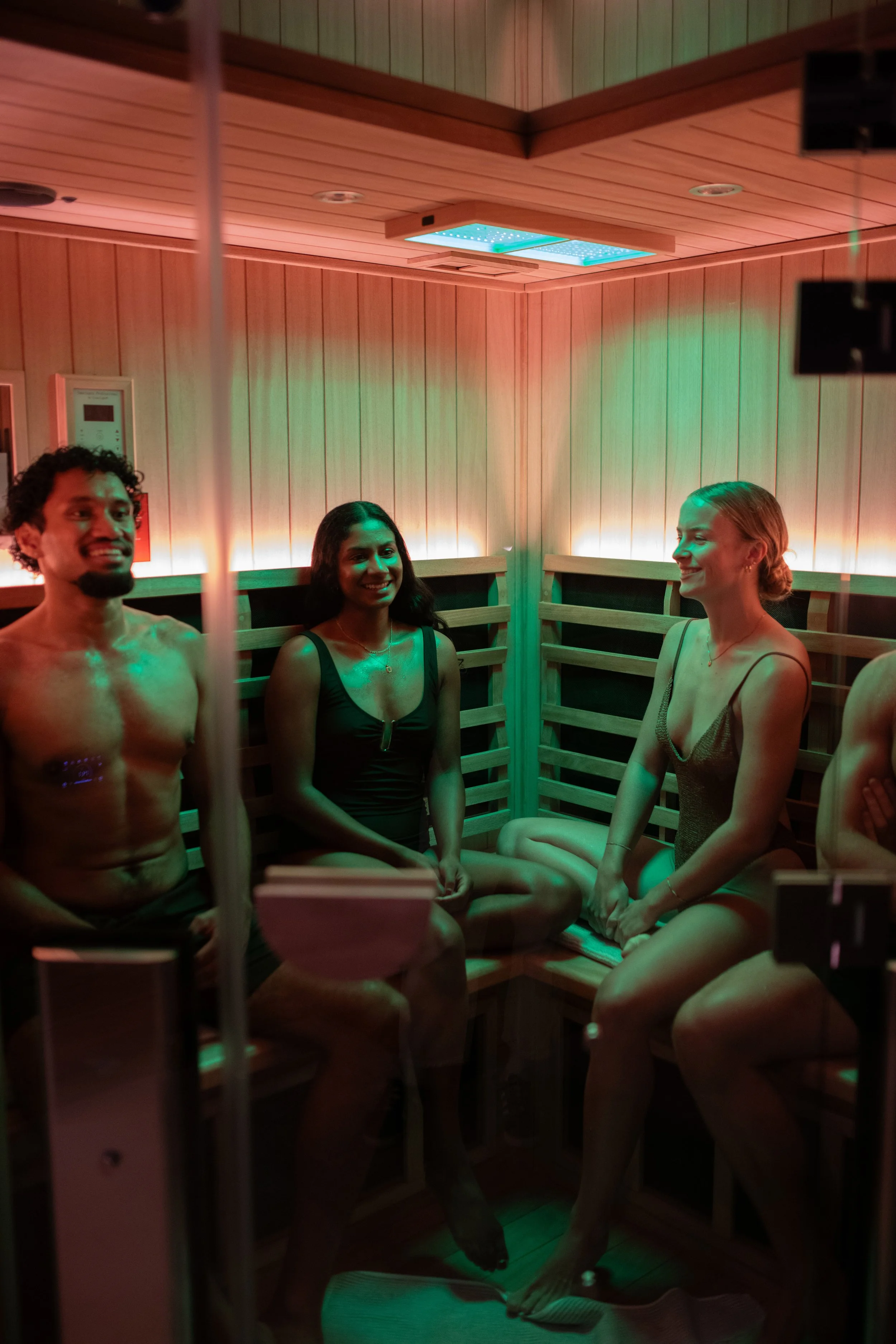 People sitting inside a wooden sauna, smiling and talking, with calm, colourful lighting.