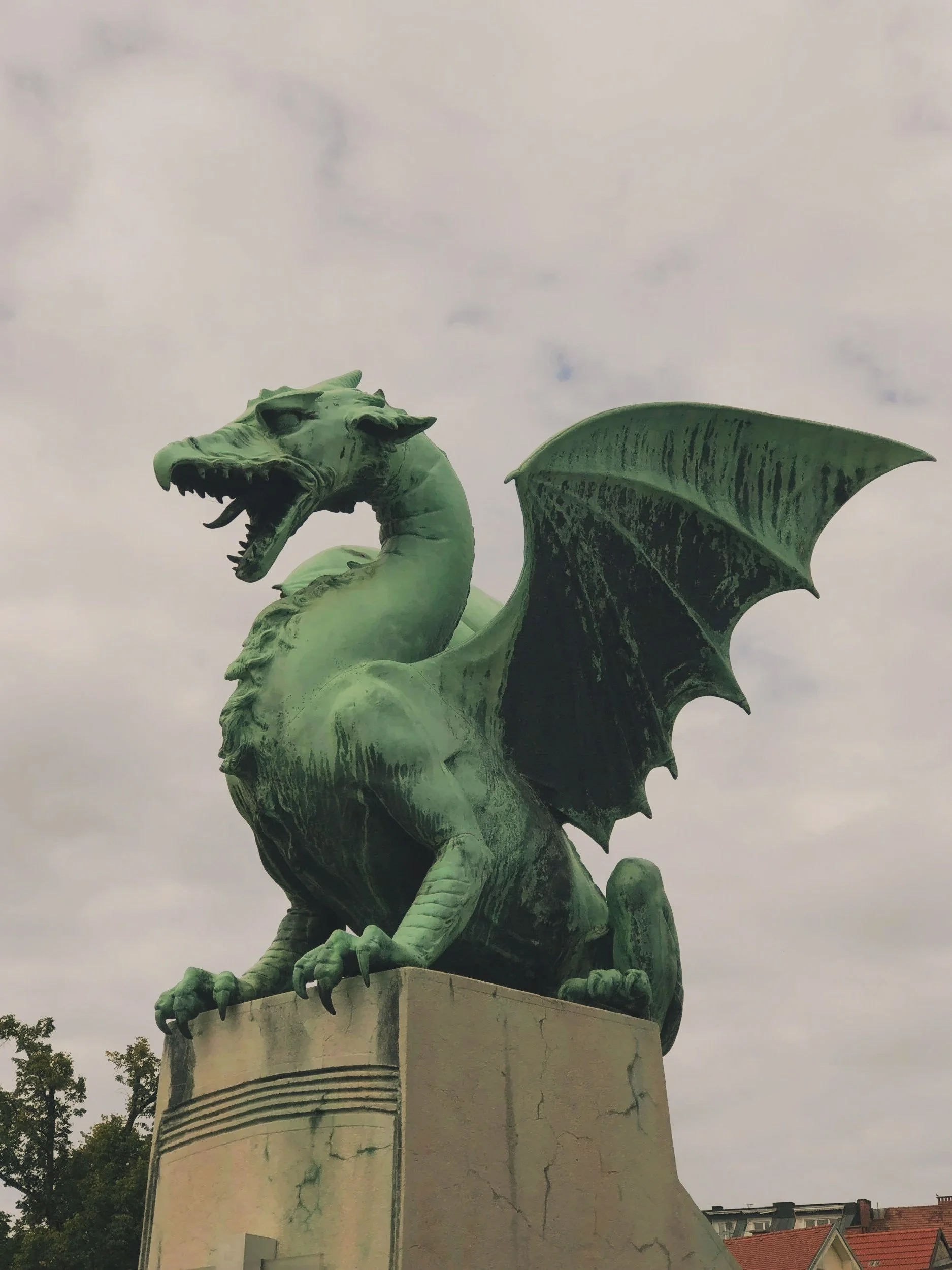 A green dragon statue with wings and an open mouth, mounted on a tall pedestal.