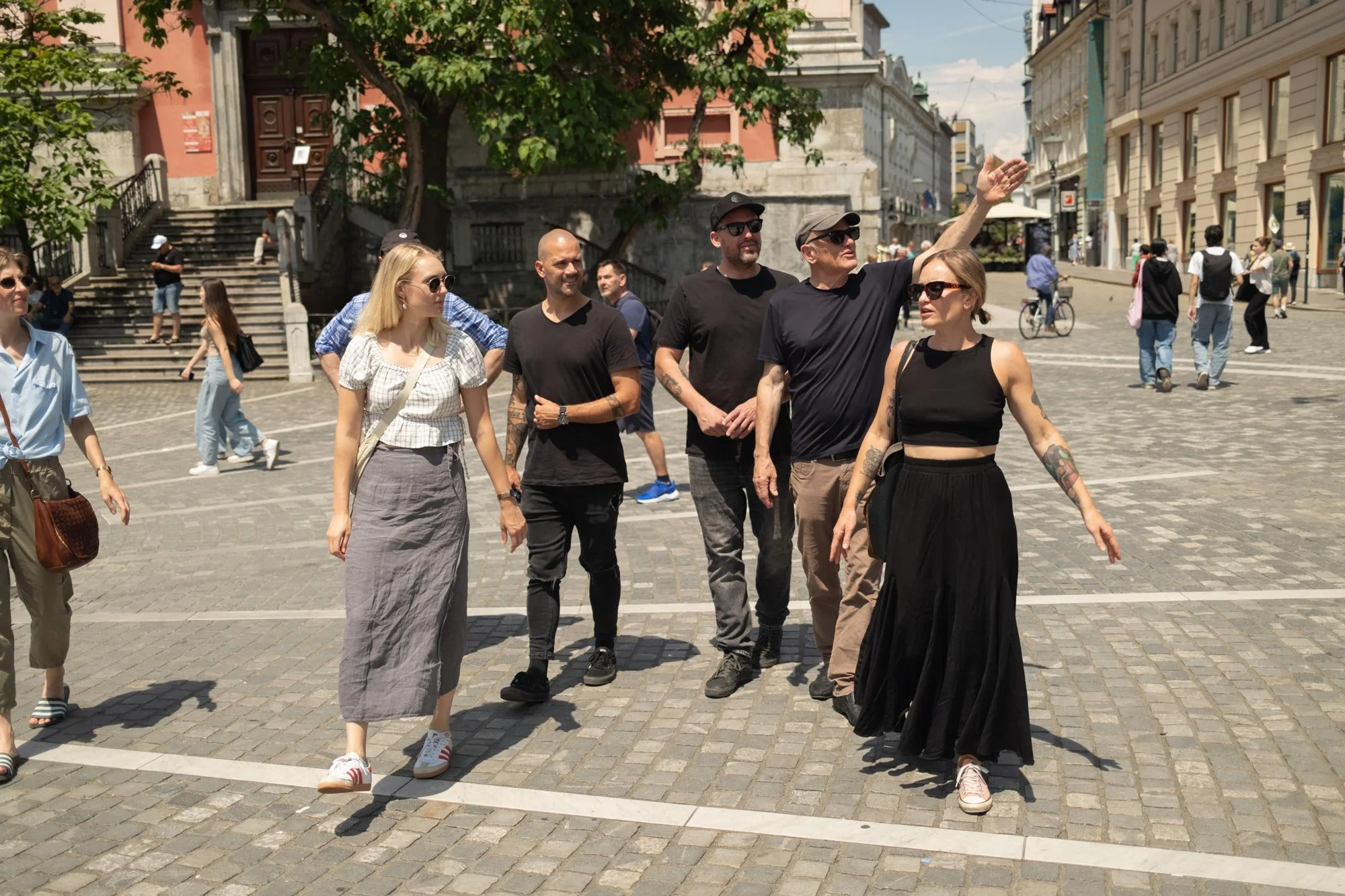 Group of diverse people walking outdoors in a city square, with one man gesturing as he talks, surrounded by historic buildings and a staircase