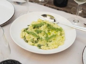 Plate of mashed potatoes with green vegetables, served with a spoon on a table with wine glasses.
