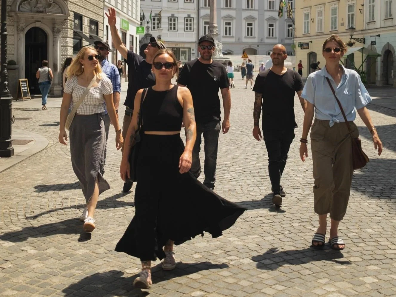 A group of seven people walking on a cobblestone street in an urban area with European-style buildings in the background.