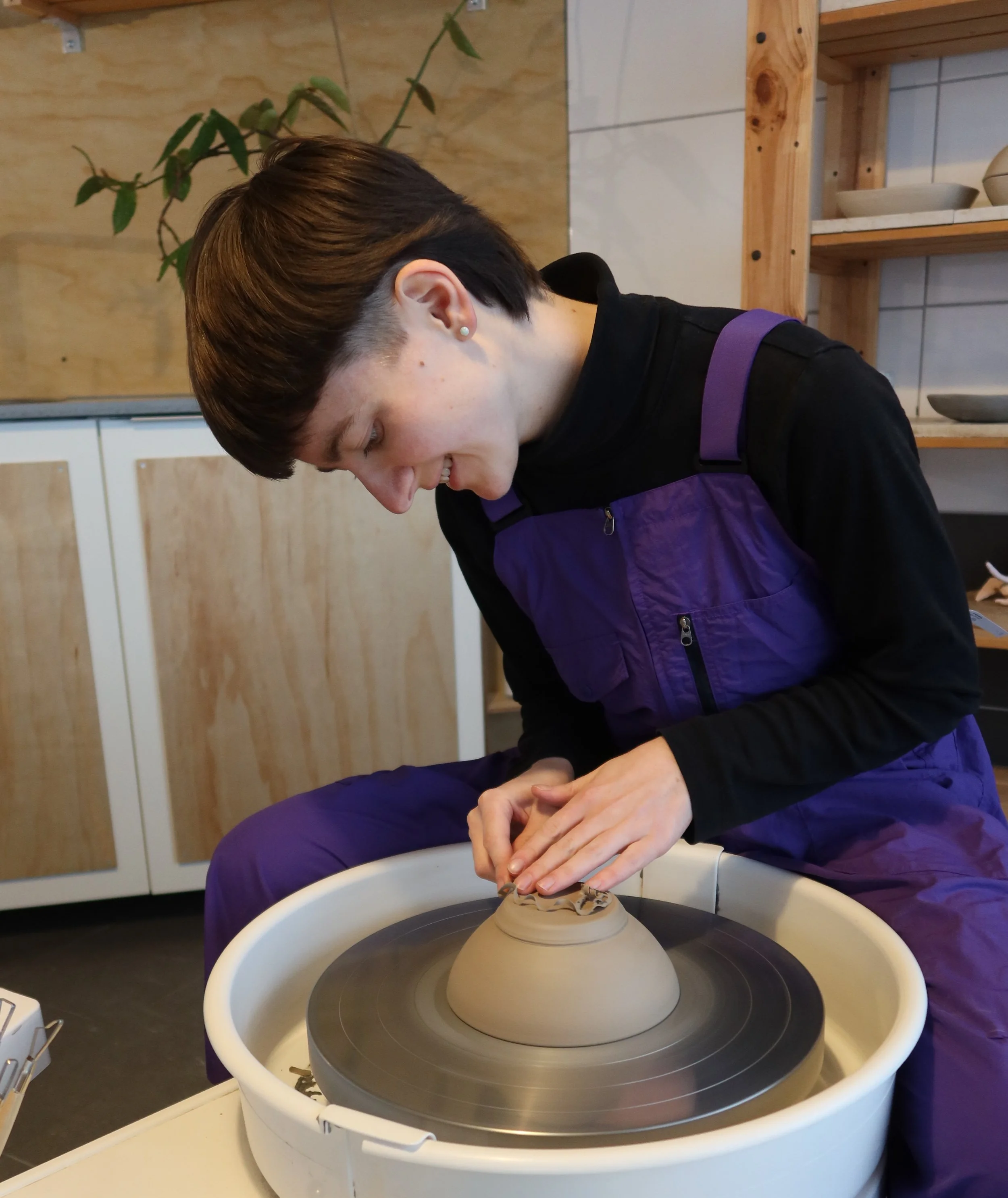 Eine junge Person beim Töpfern an der Drehscheibe in einer Werkstatt.