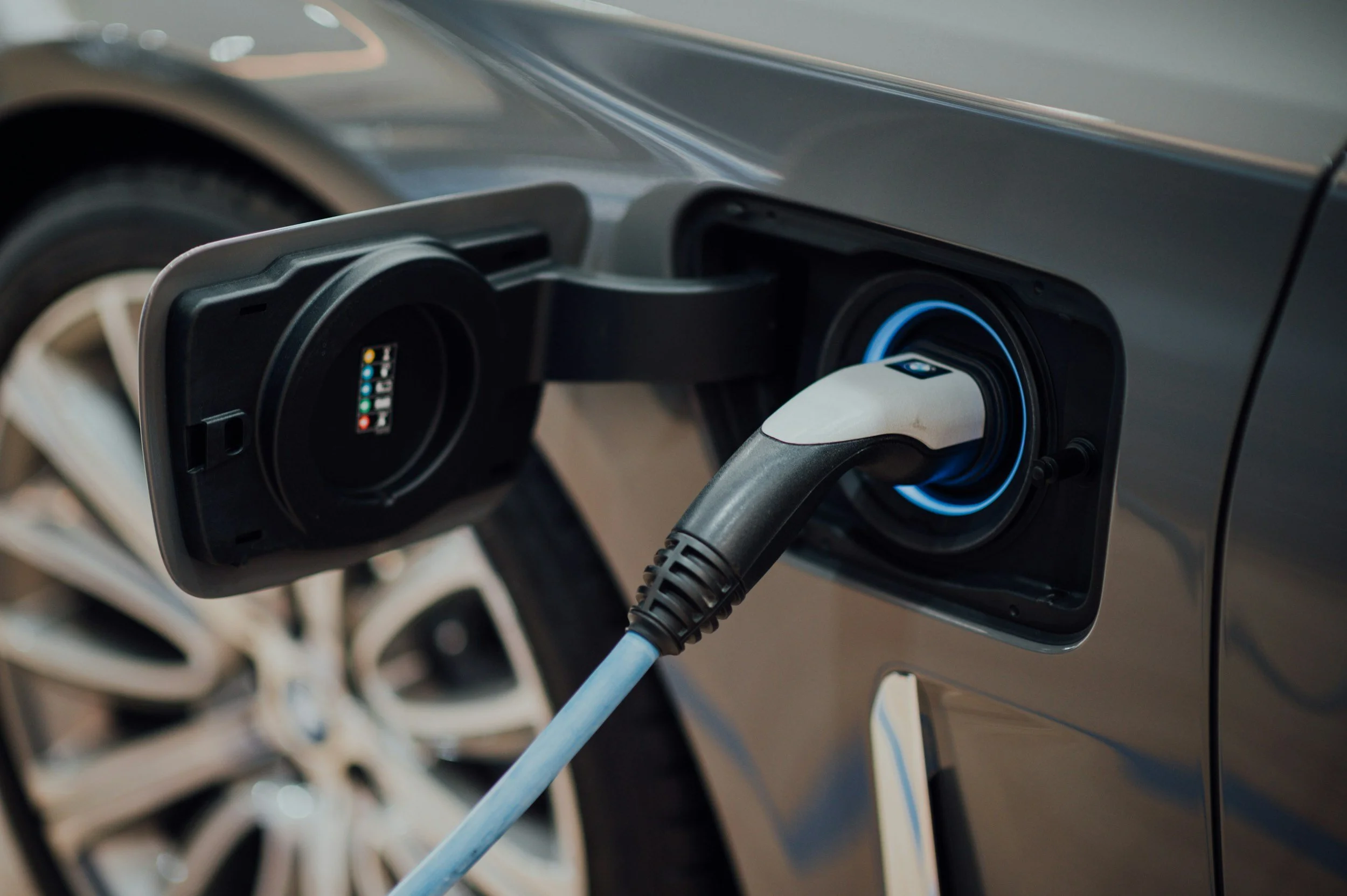 Close-up of an electric car being charged, with the charging cable plugged into the vehicle's charging port on the side of the car.