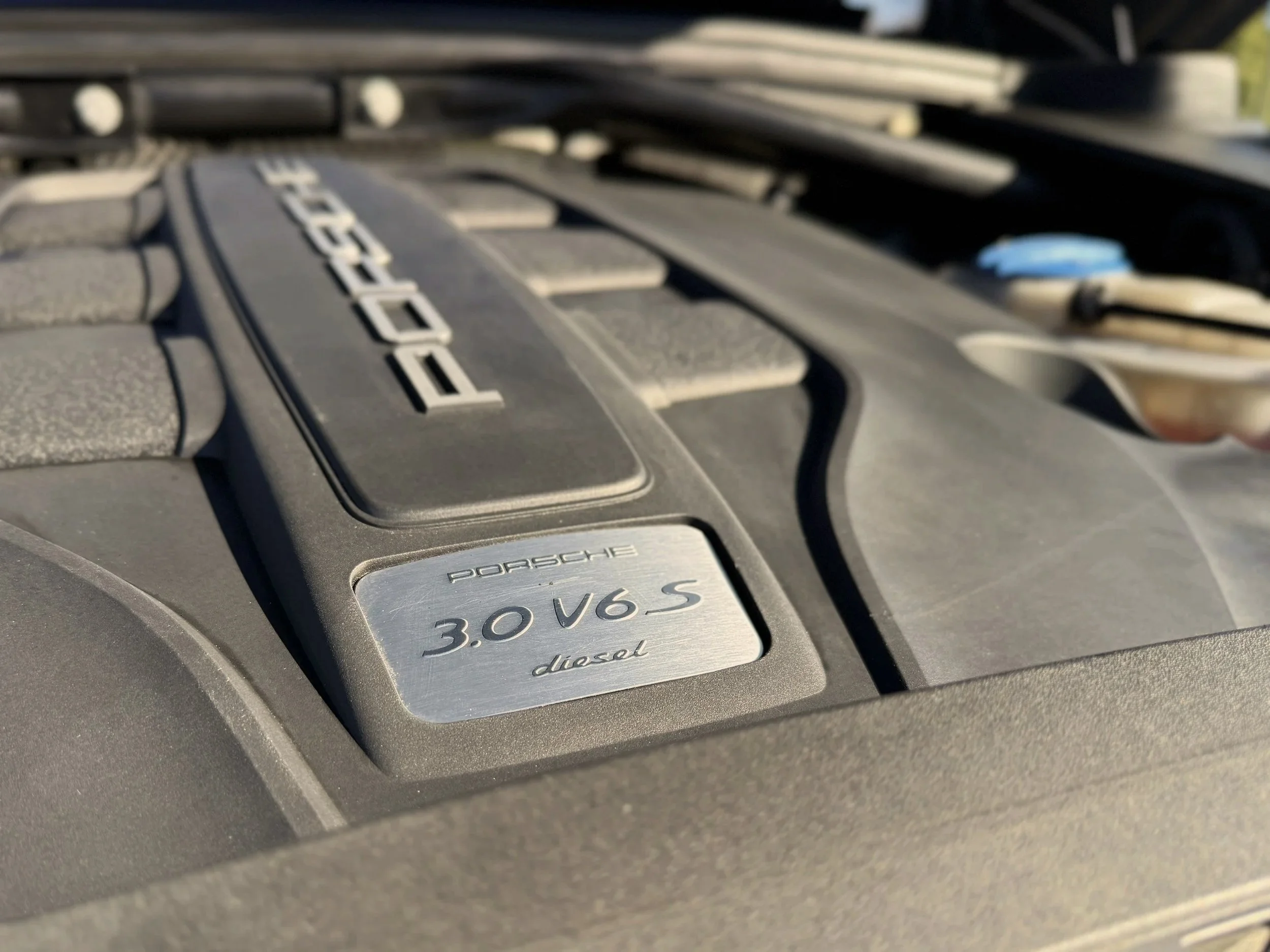 Close-up of a Porsche engine cover with a metal badge that reads 'Porsche 3.0 V6 S Diesel'.