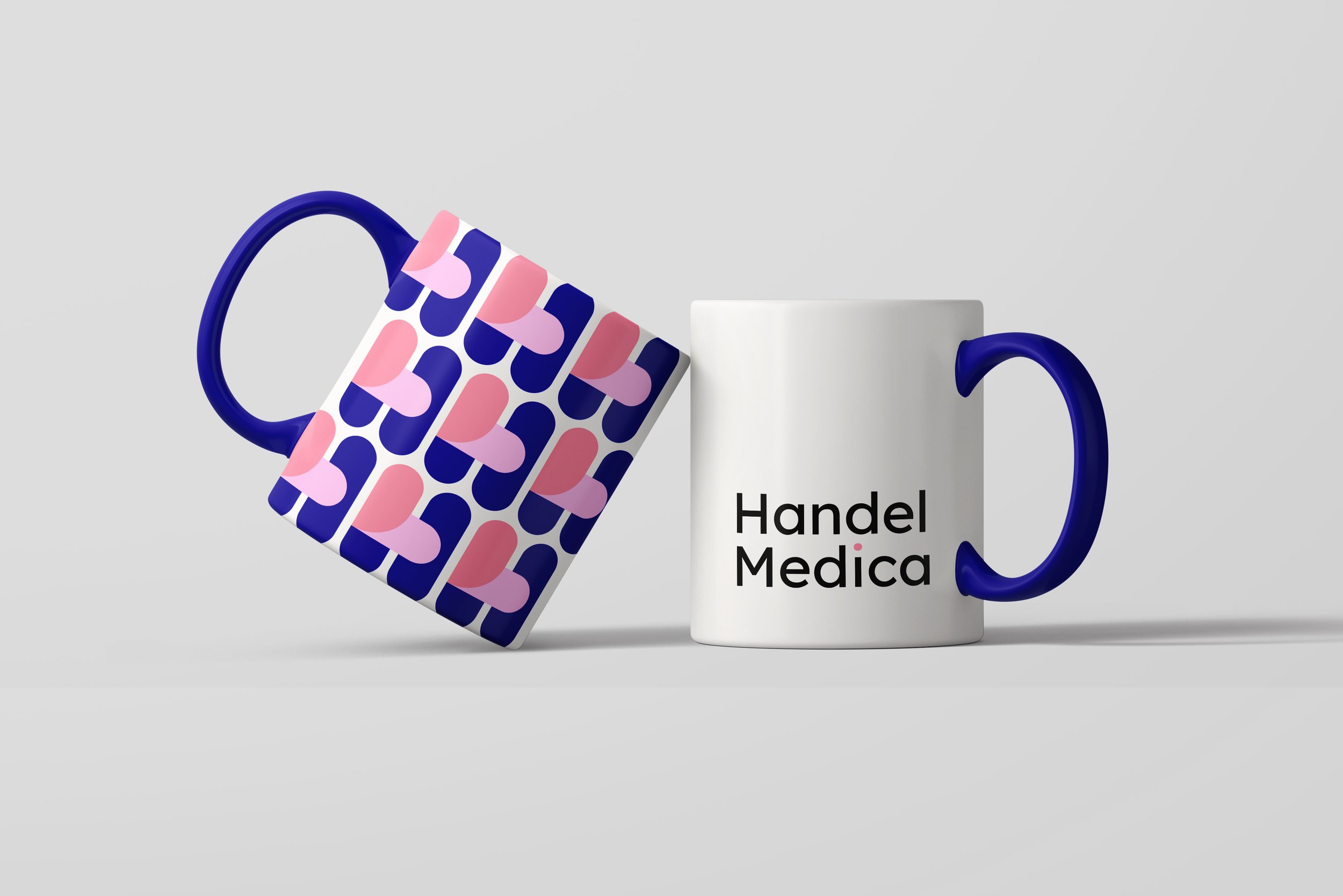 Two white ceramic mugs, one on its side with a blue handle and a patterned exterior and the other upright with a handle and text reading 'Handel Medica'.