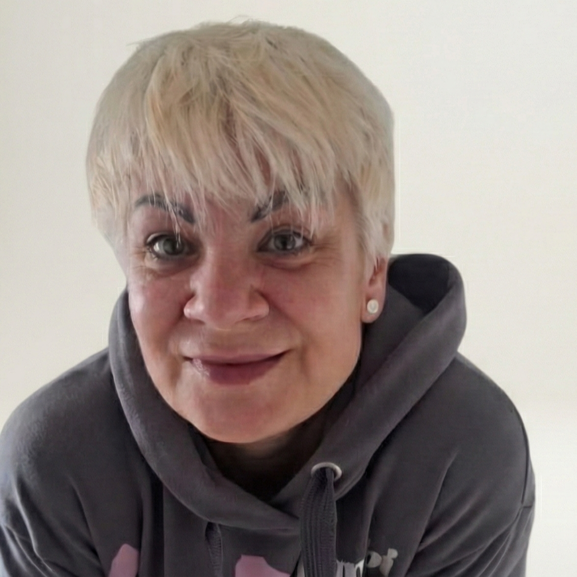 Eine Person mit kurzen blonden Haaren, grauen Augen und einem grauen Hoodie, lächelnd in die Kamera schauend.