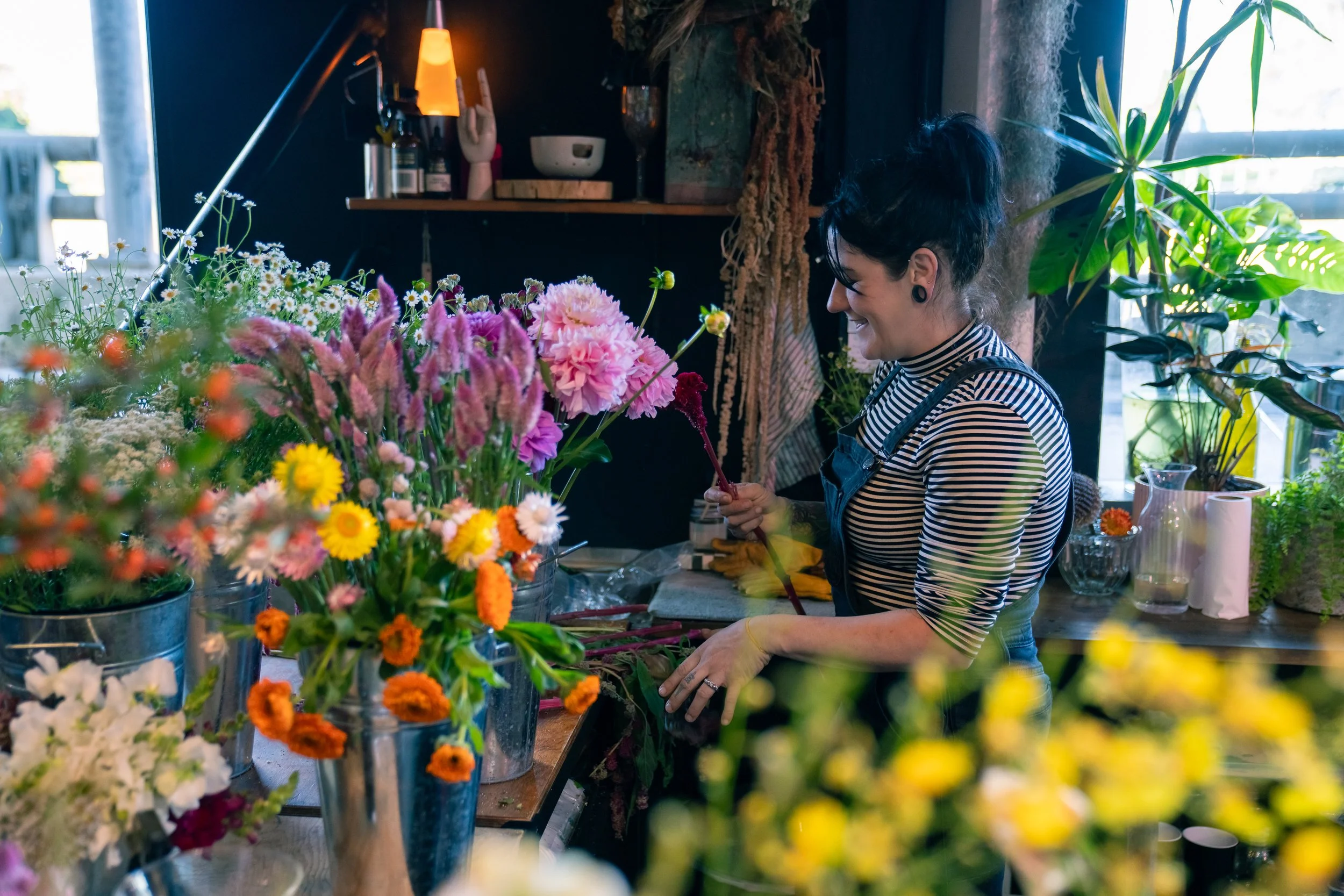 A florist wearing a striped shirt and black overals, conditioning seasonal blooms. Photo by Trish evans photography
