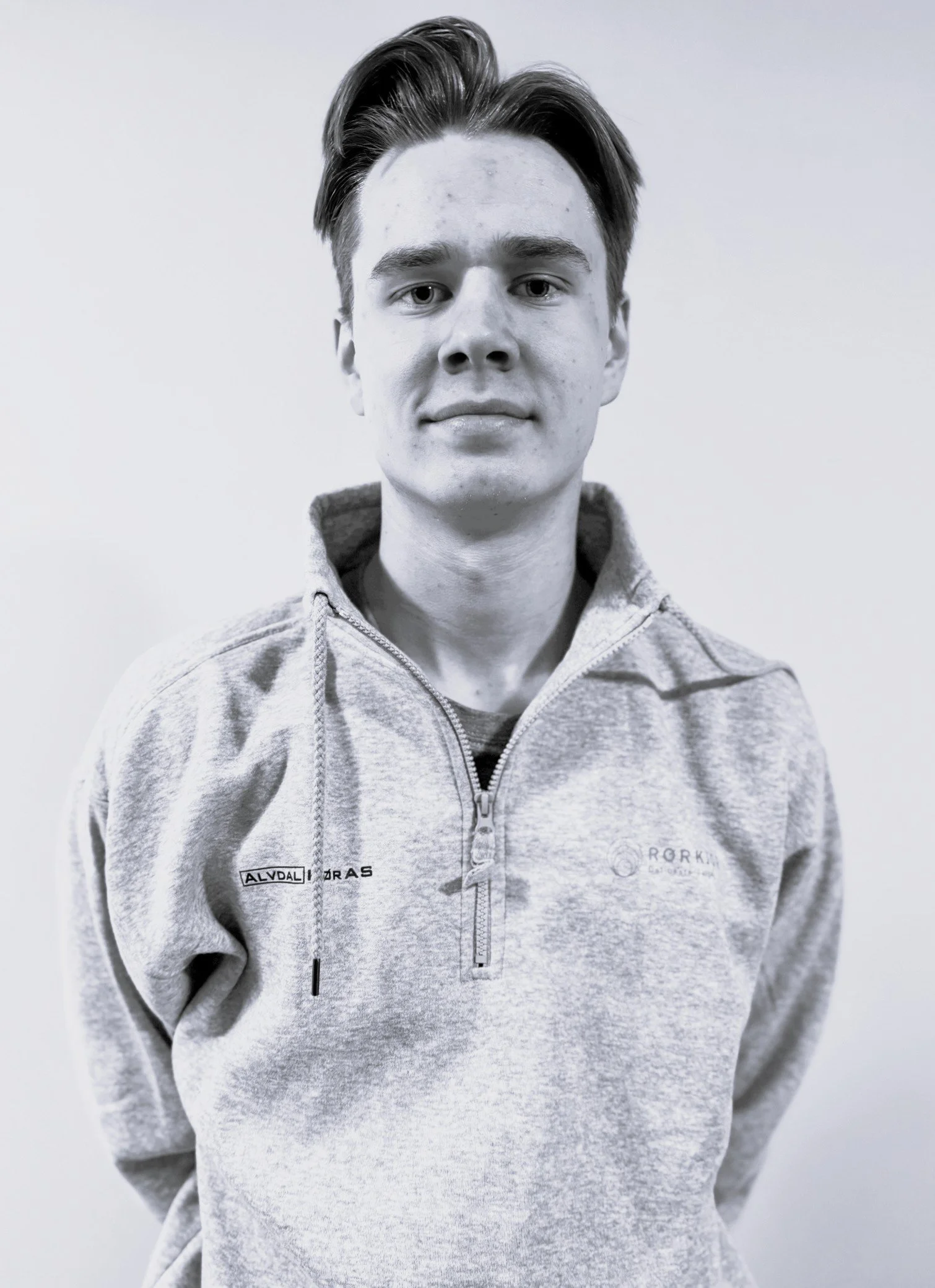 Lidvin Granrud Hokstad. Svart-hvitt bilde av en ung mann med kort, stylet hår som ser direkte inn i kamera. Han har på seg en lys grå zip-up hettegenser med logoer og teksten 'ALVDAL RØR' og 'RØRKJØP' på genserens bryst. Bakgrunnen er enkel og hvit.