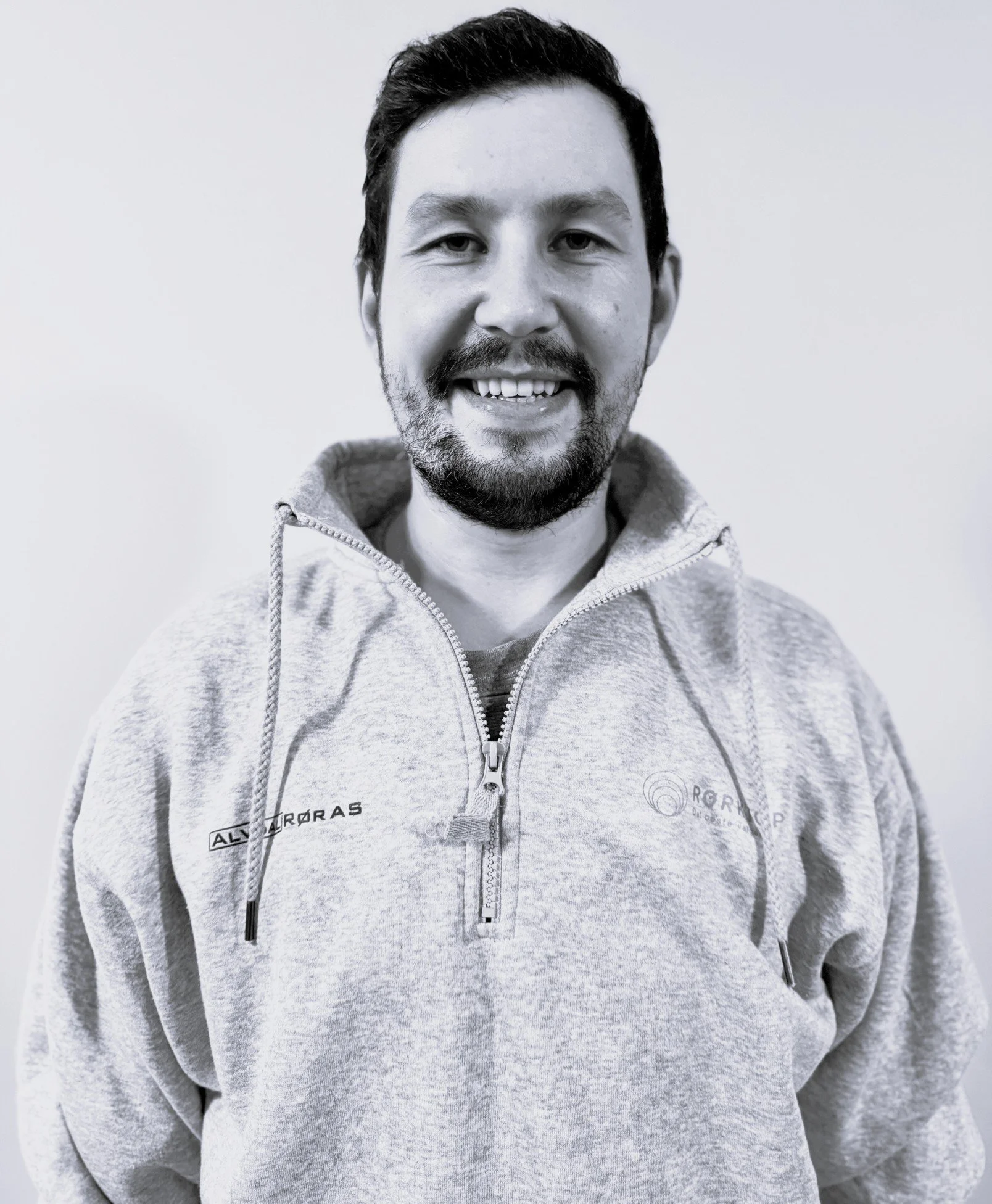 Nicolas Lopez Vega. Et portrett av en mann med mørkt hår og skjegg, iført en lys grå hettegenser med glidelås, mot en enkel lys bakgrunn.