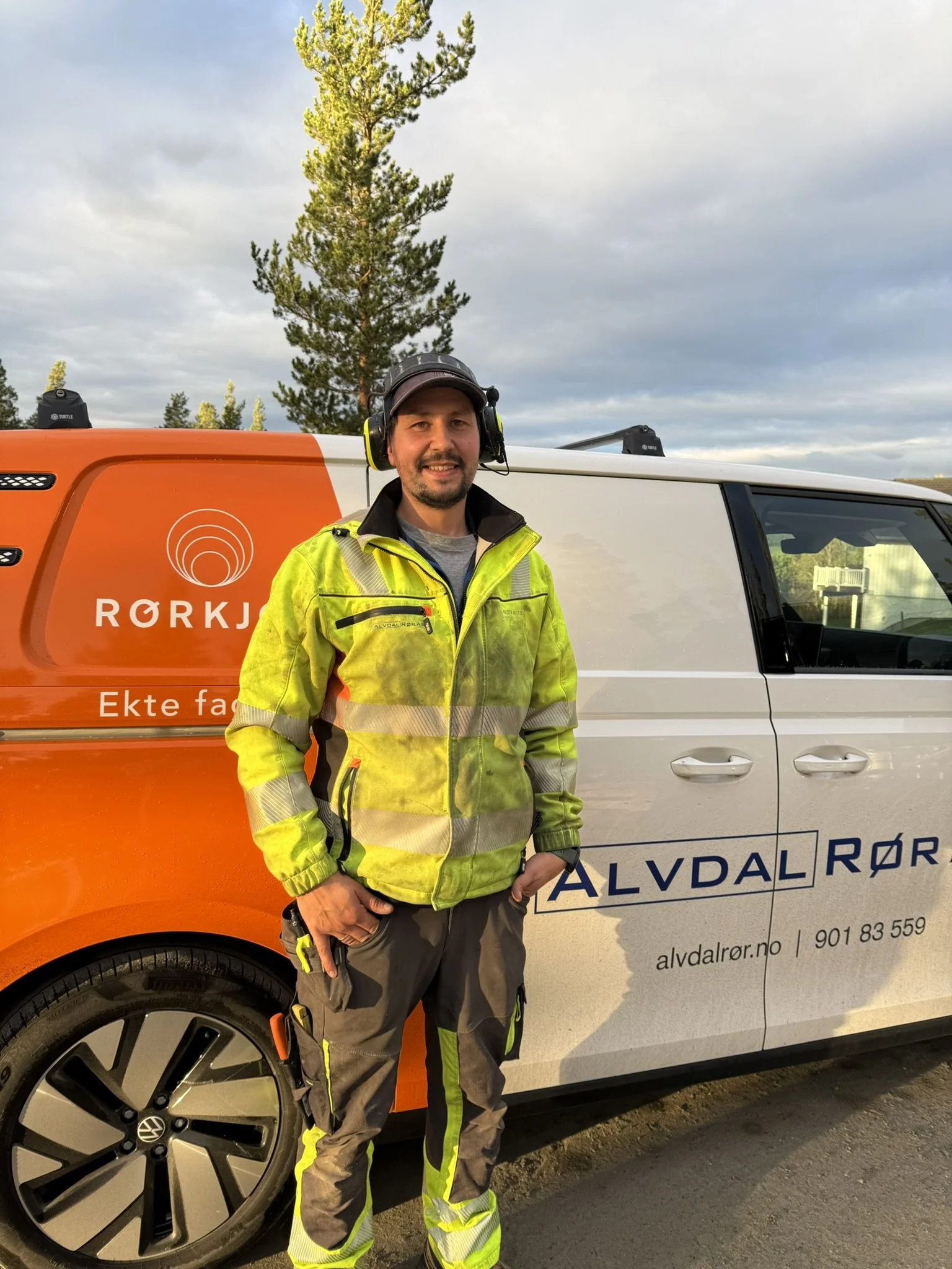 Nicolas Lopez Vega. En mann i høyt synlig arbeidsantrekk står foran en varebil med teksten "Rørkompetanse" og "Ekte fagfolk". Varebilen er hvit med oransje og blå dekor, og det er trær og en overskyet himmel i bakgrunnen.