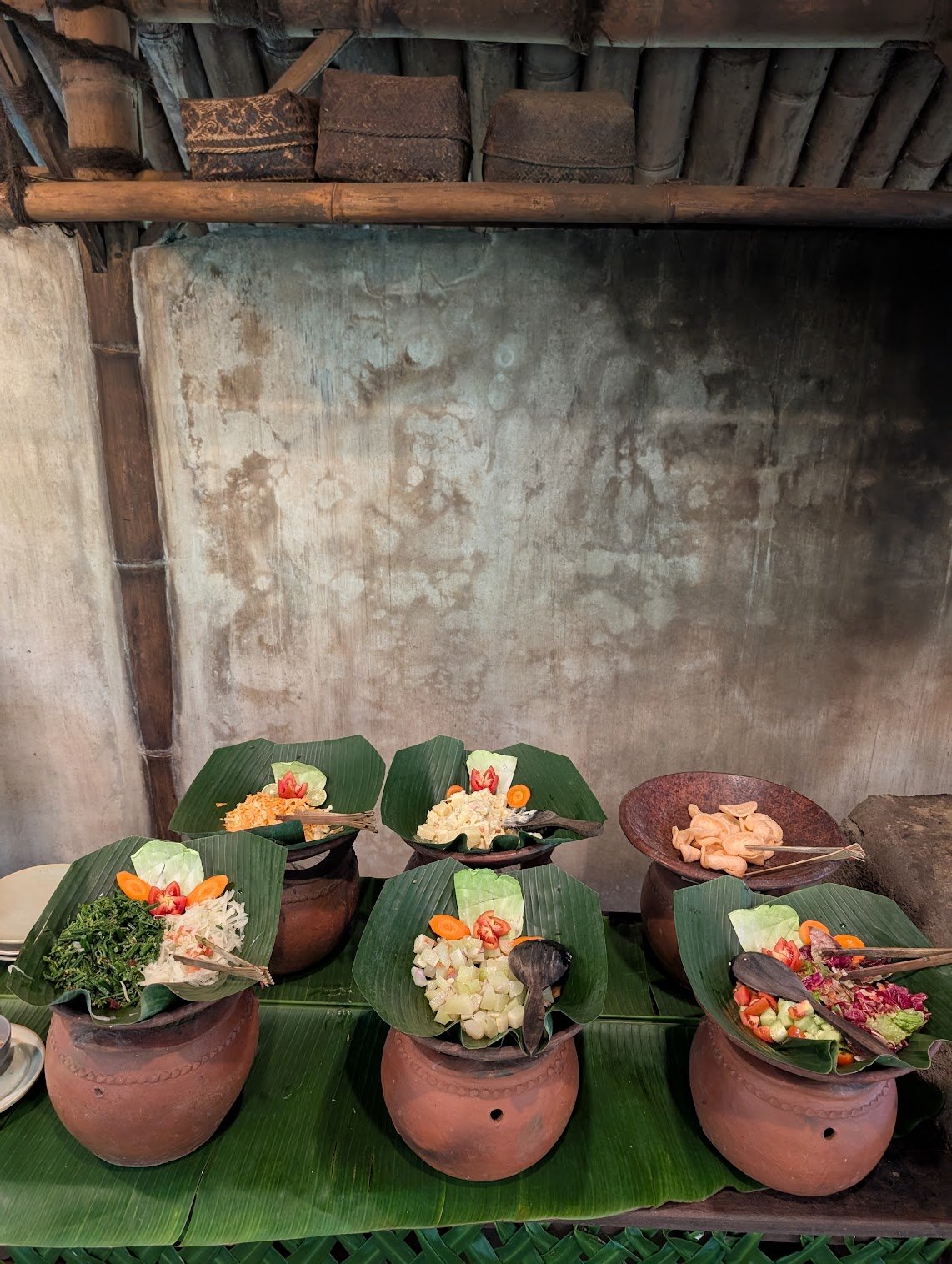 Traditional Asian food arranged in clay pots with banana leaf covers, including salads and appetizers at a rustic setting at Bamboo restaurant in Munduk.