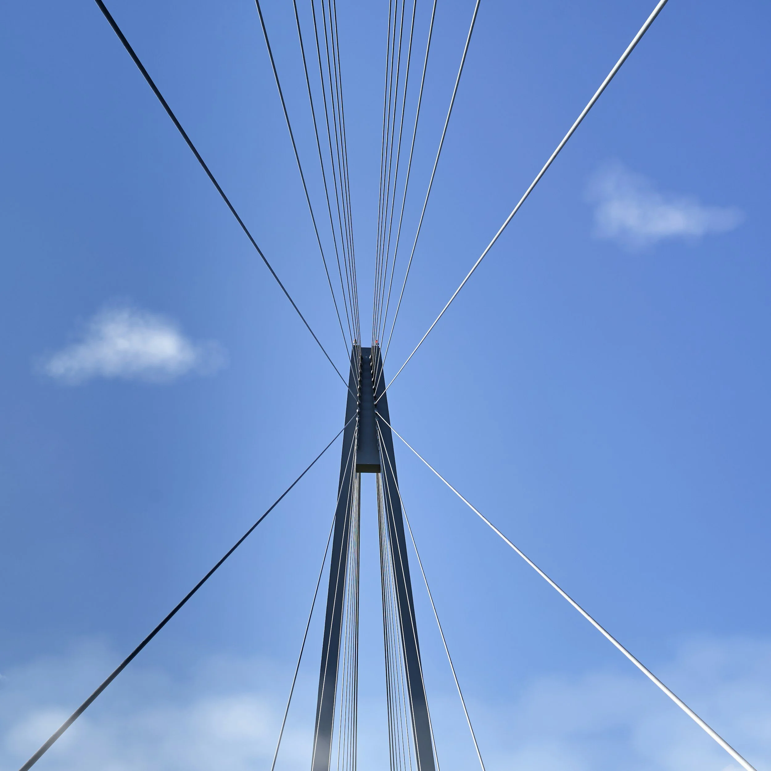 View from below of a tall cable car tower with multiple steel cables extending into the blue sky with a few clouds.
