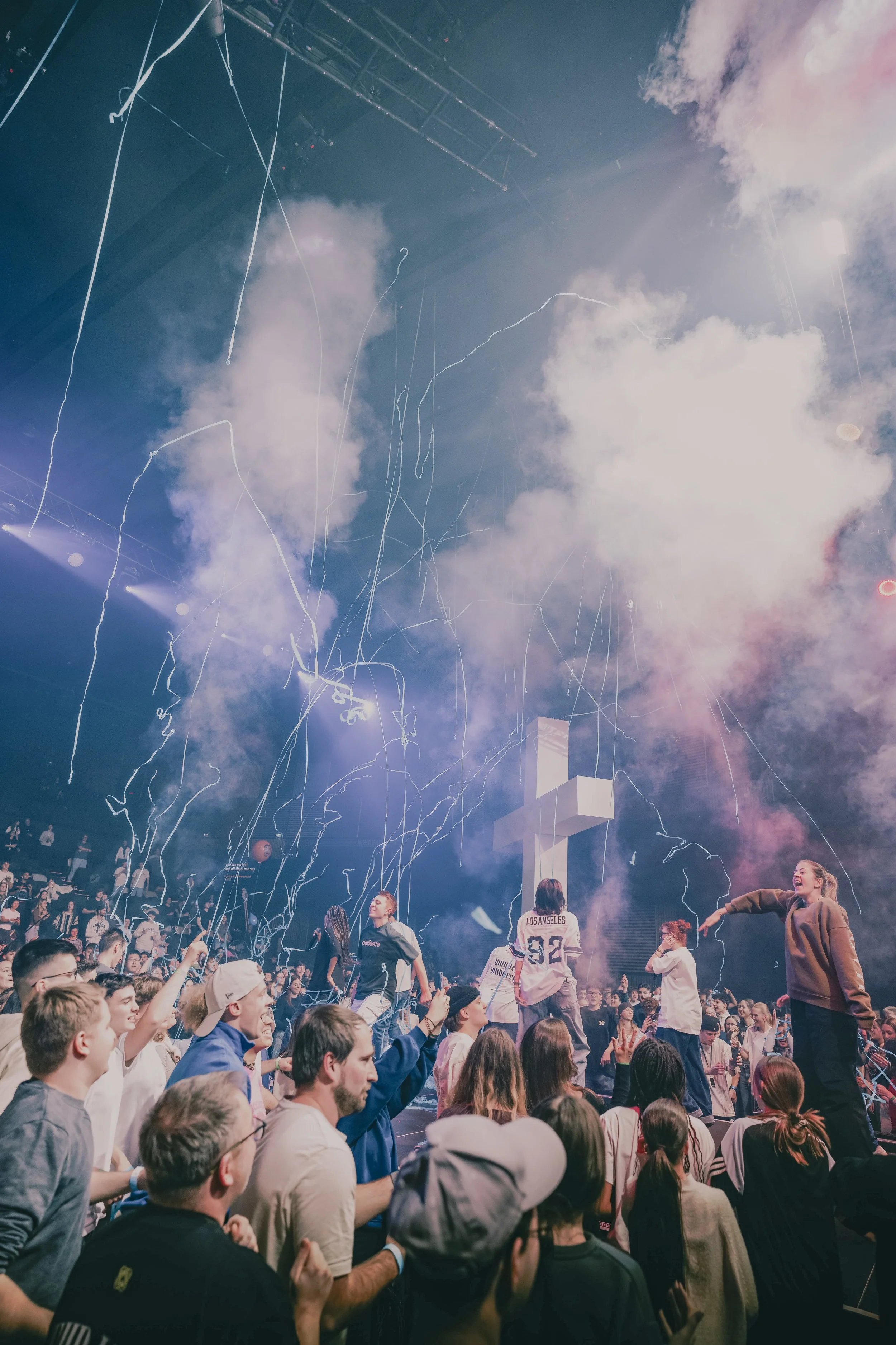Menschen feiern auf einer Party vor einer Bühne mit Rauch und Licht, Konfetti und Streamern in der Luft.