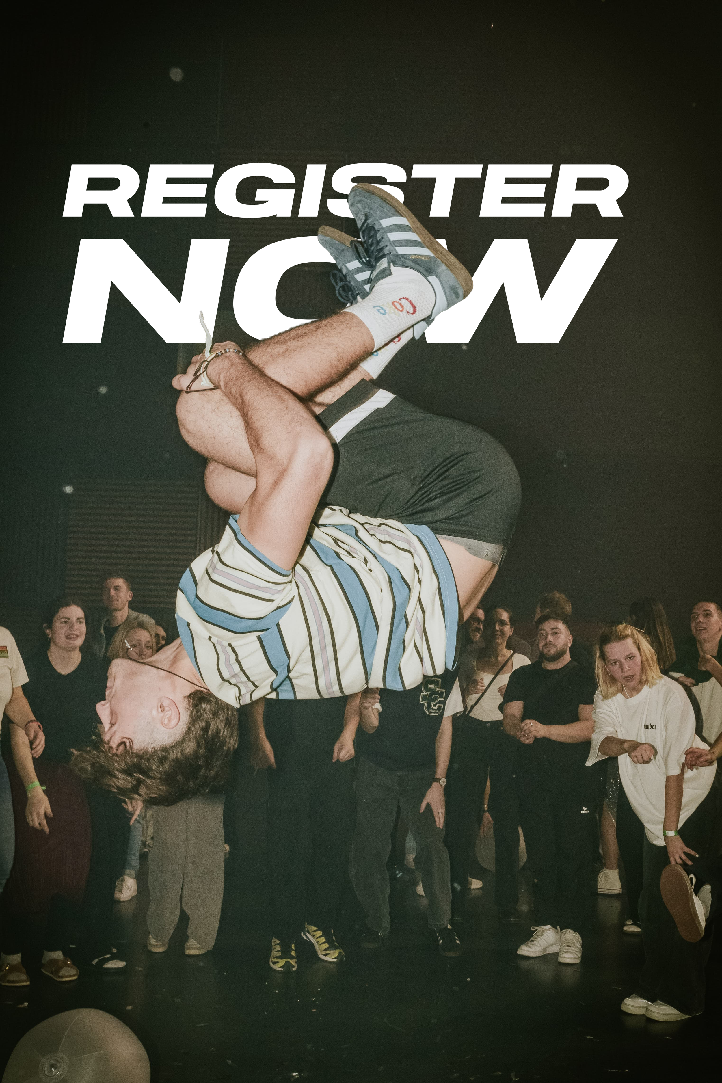 Ein Mensch führt einen Handstand unter einer großen, weißen Schrift mit der Aufschrift 'REGISTER NOW' in einer Menschenmenge durch.