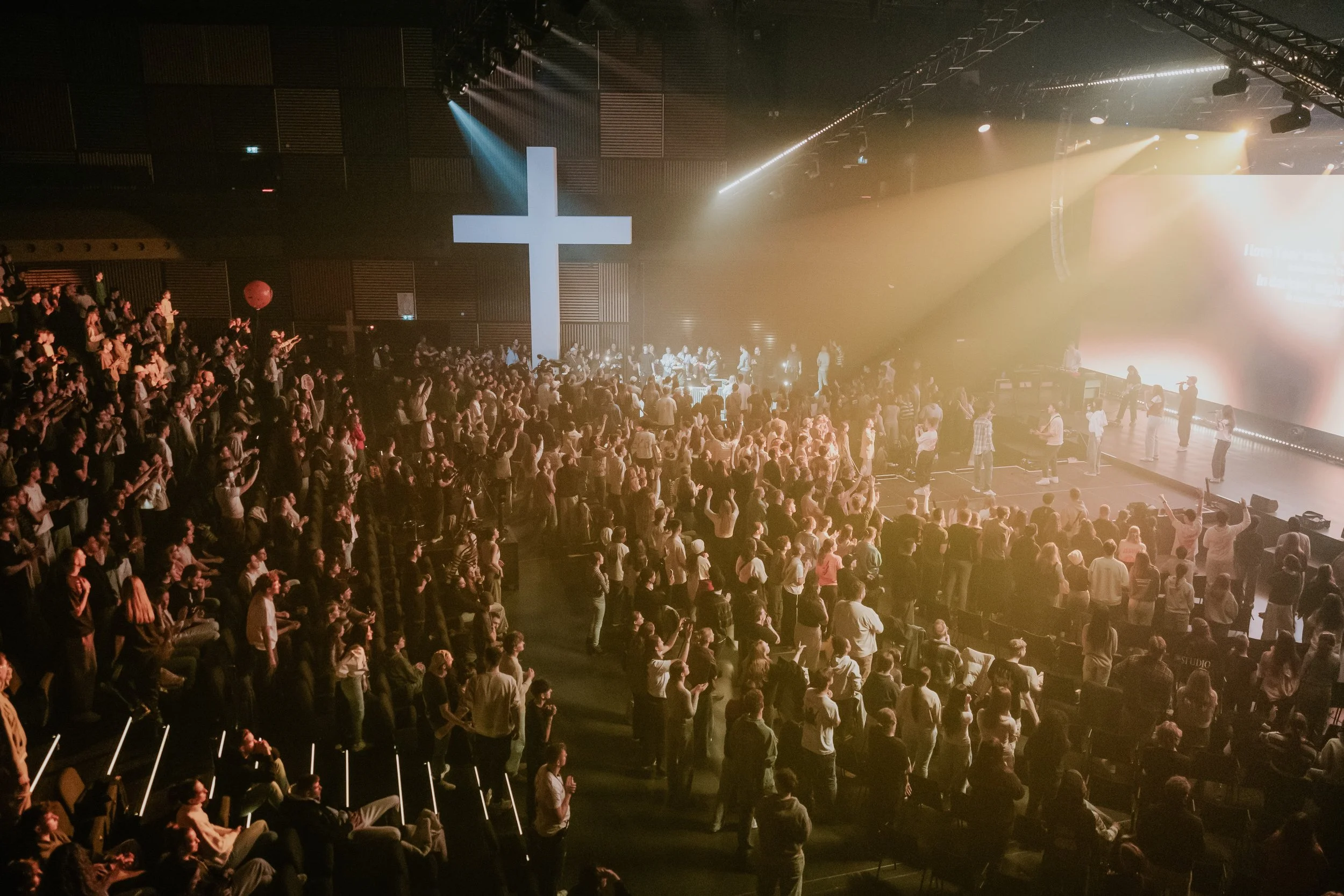 Bunt beleuchtete evangelische Kirche mit einer großen Menschenmenge im Saal, einer großen weißen Kreuz auf der Bühne und einem großen Bildschirm im Hintergrund.