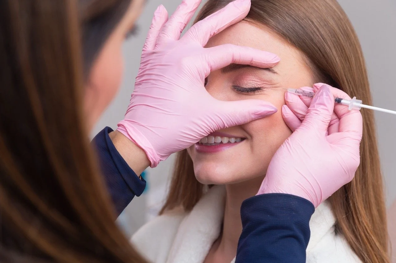A healthcare worker administering a cosmetic injection near a woman's eye.