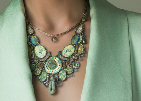 Close-up of a person wearing layered, colorful gemstone jewelry and a mint green blazer.