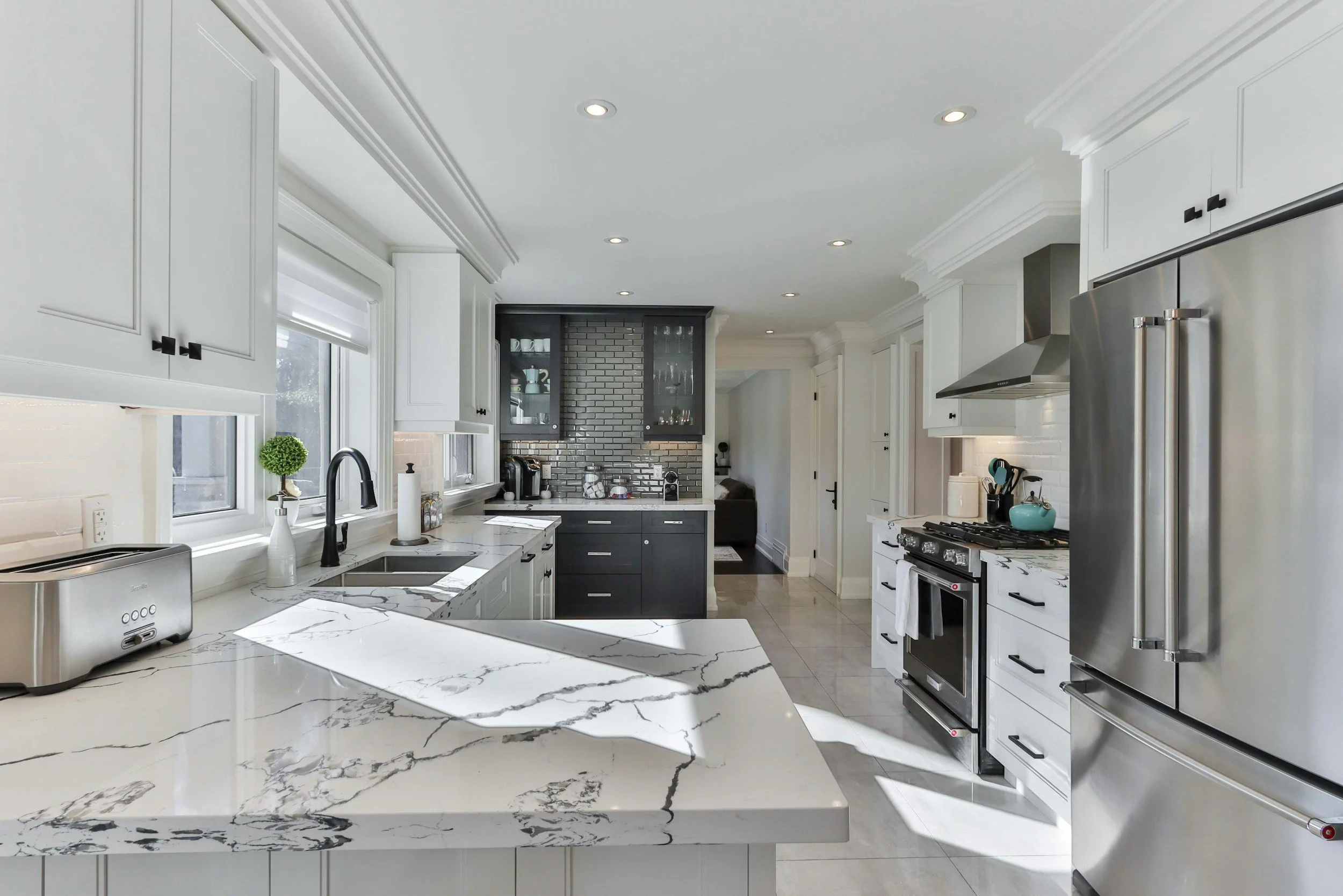 Modern kitchen with white cabinets, marble countertop, stainless steel appliances, and a black brick backsplash. regular house cleaning