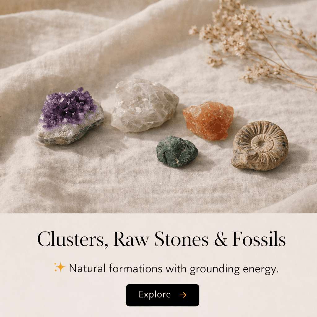 A collection of five different raw stones and fossils on a beige fabric surface, with a sprig of dried white flowers in the background.