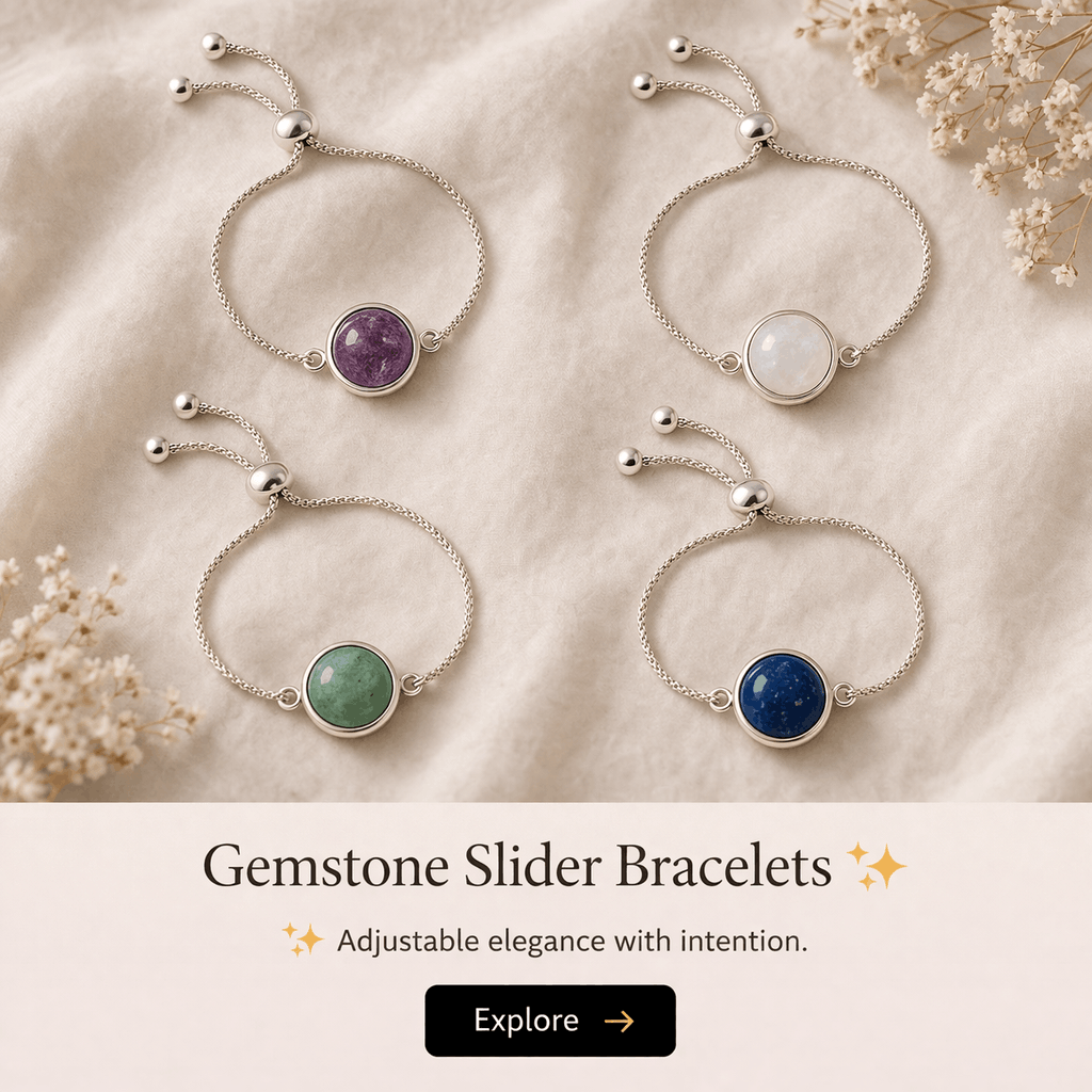 Four gemstone slider bracelets with adjustable chains on a beige fabric surface. Each bracelet has a circular gemstone in different colors: purple, white, green, and blue, with small decorative silver beads at the ends of the chains. Flowers are visi