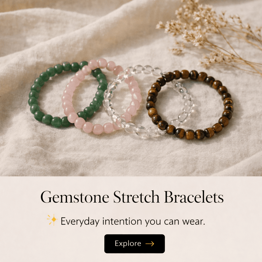 Set of four gemstone stretch bracelets in green, pink, clear, and brown beads, resting on beige fabric with dried flowers nearby.