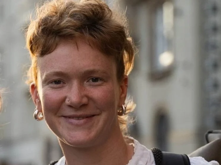 Junge Frau mit roten Haaren, Piercings und Schmuck, lächelnd auf der Straße.