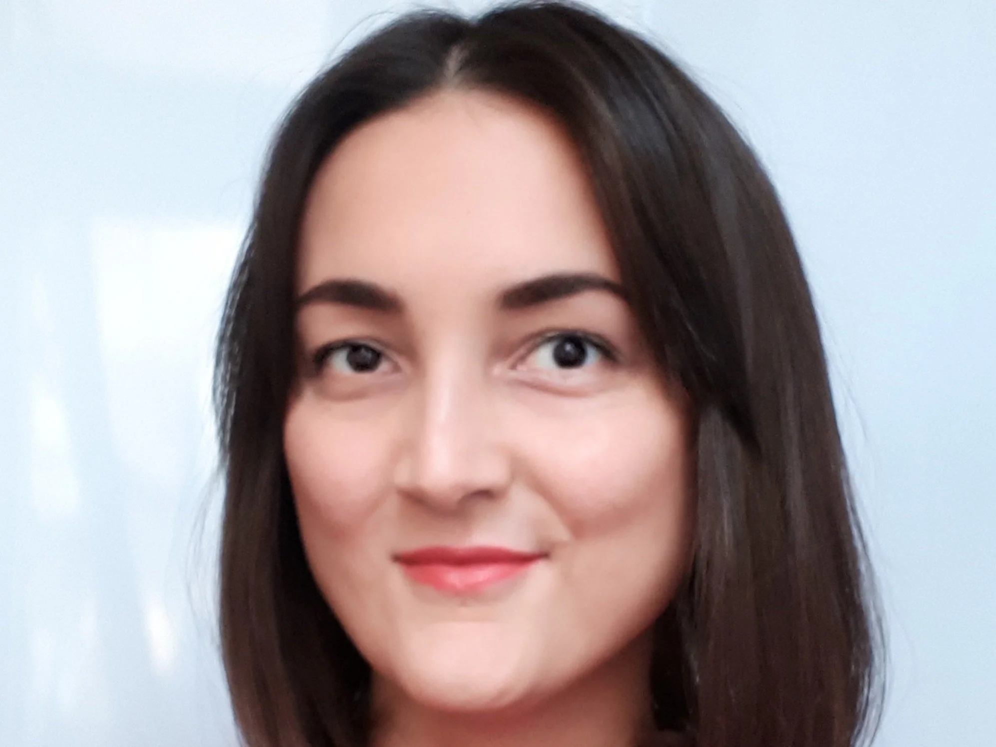 Nahaufnahme eines jungen Frau mit braunen Haaren und heller Haut, lächelnd, gegen einen blauen Hintergrund.