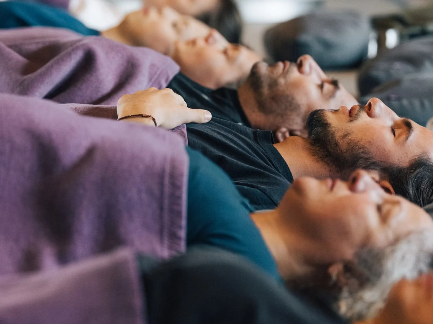 Menschen liegen nebeneinander mit geschlossenen Augen, scheinbar in einer Entspannungs- oder Meditationssitzung.