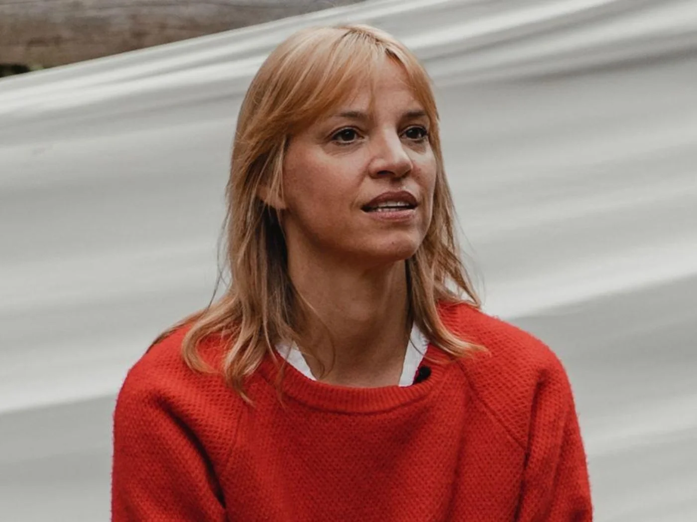 Eine Frau mit roten Haaren und rotem Pullover steht vor einer grauen Wand.