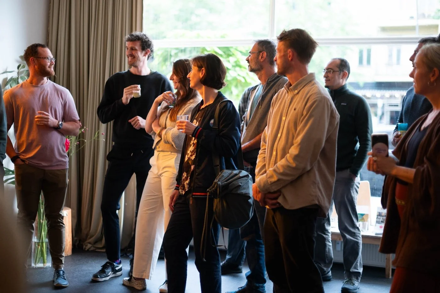 Menschen versammeln sich in einem Raum, unterhalten sich und trinken Getränke, während sie eine Präsentation oder Veranstaltung verfolgen.