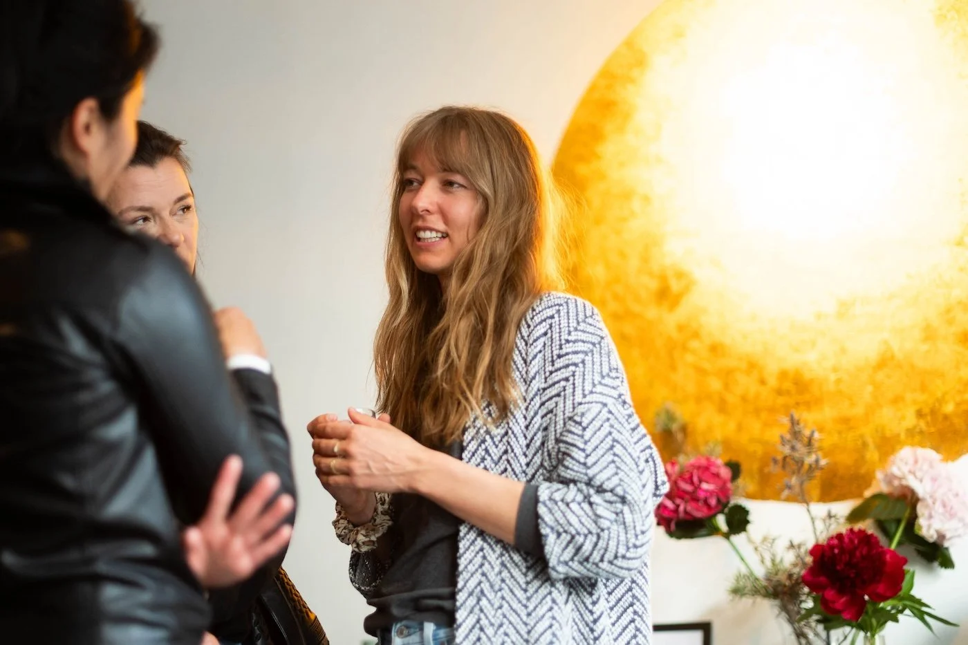 Drei Menschen unterhalten sich in einem Raum mit einer goldenen Wand und Blumen im Hintergrund.