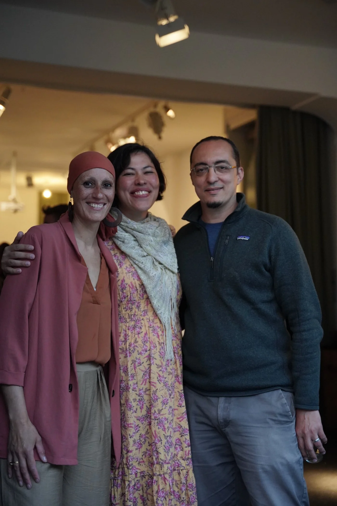 Drei Menschen, zwei Frauen und ein Mann, lachen und posieren in einem Raum mit warmem Licht.
