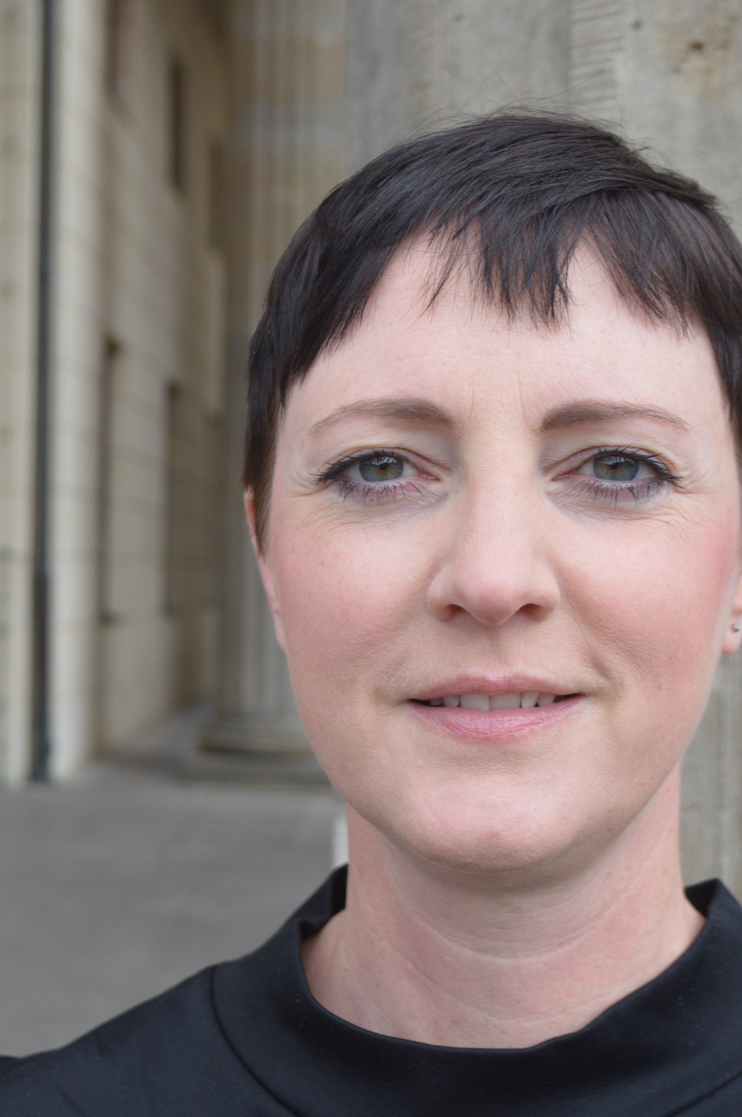 Nahaufnahme eines lachenden Frauenkopfes vor einer antiken Gebäudefront