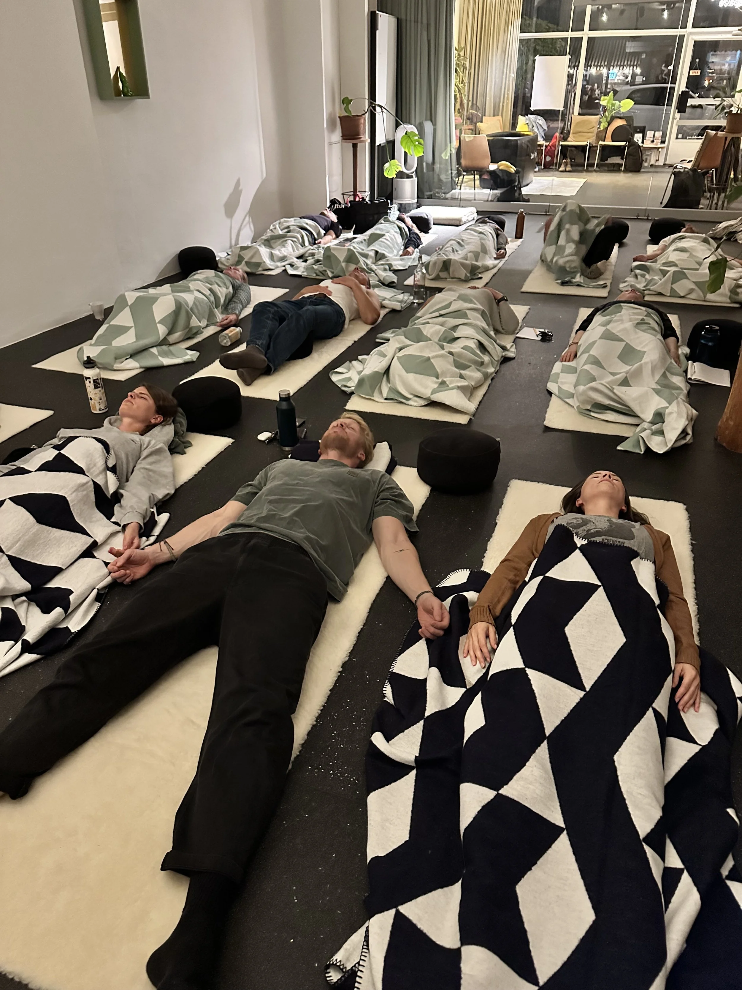 Menschen, die auf Matratzen schlafen, in einem Raum mit großen Fenstern und modernen Möbeln.